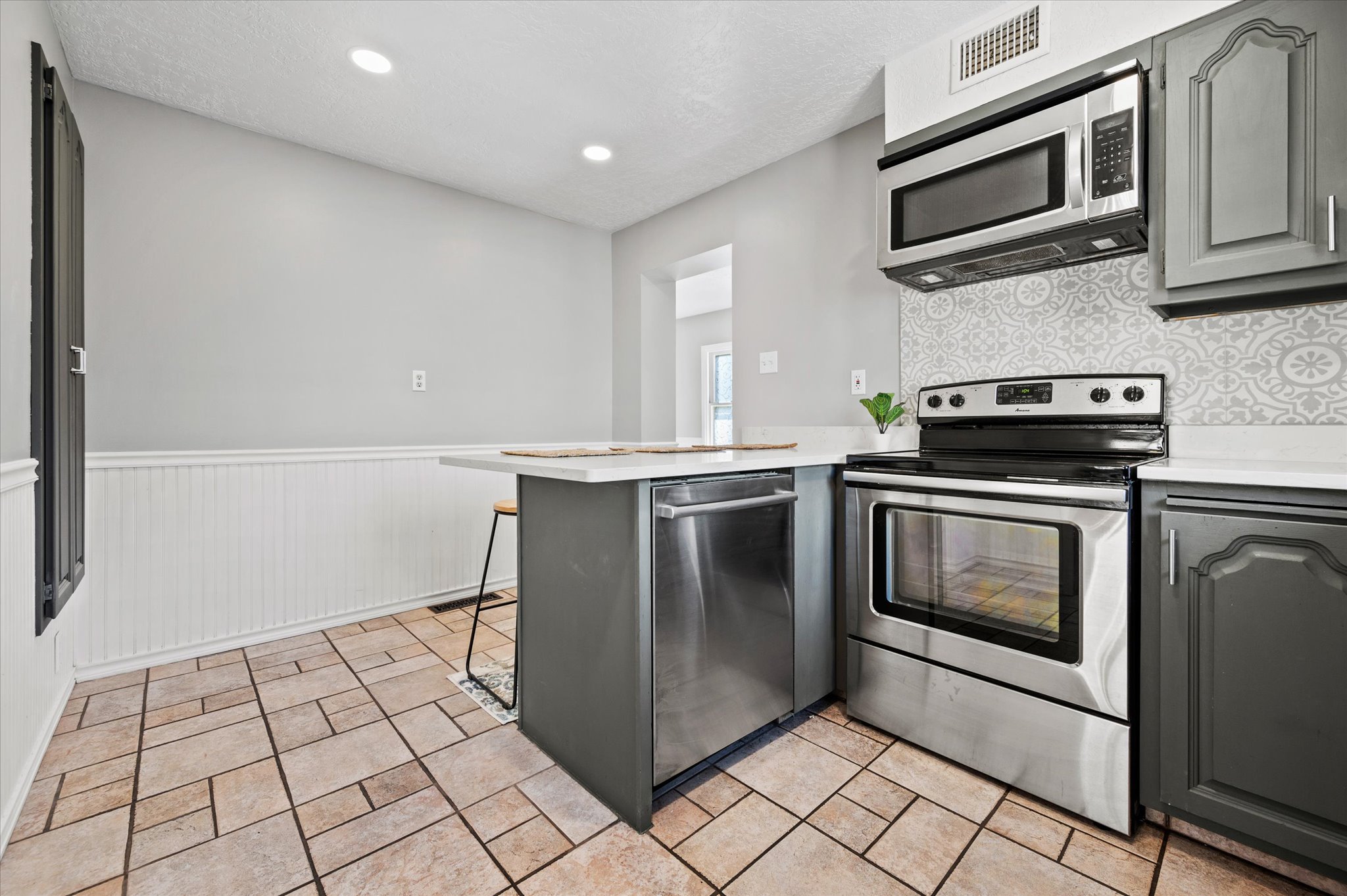 Kitchen featuring stainless steel appliances, white countertops, patterned backsplash, recessed lighting, and tile flooring