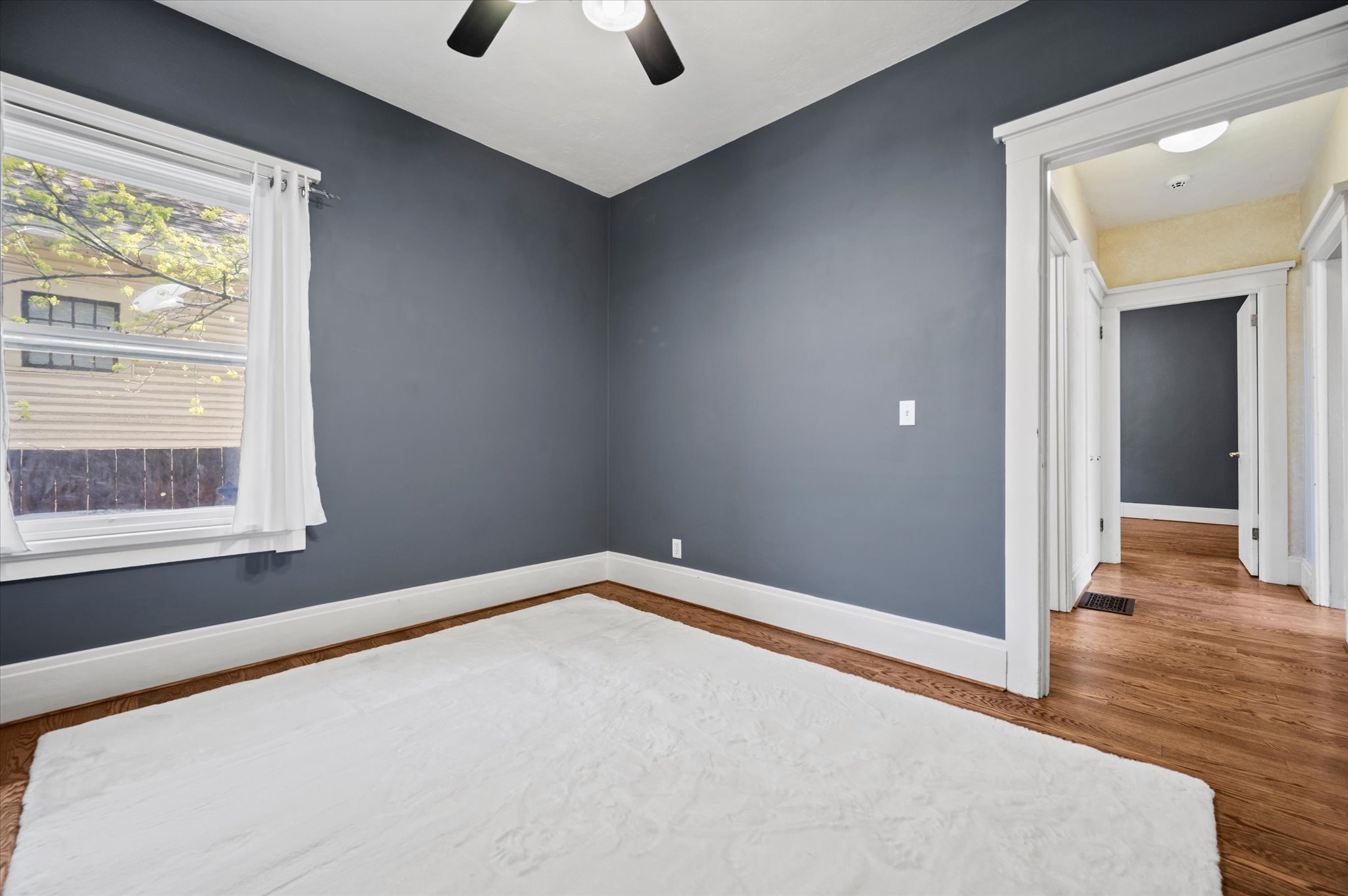 Room featuring wood-finish flooring, a ceiling fan, white baseboards, and a window with white trim