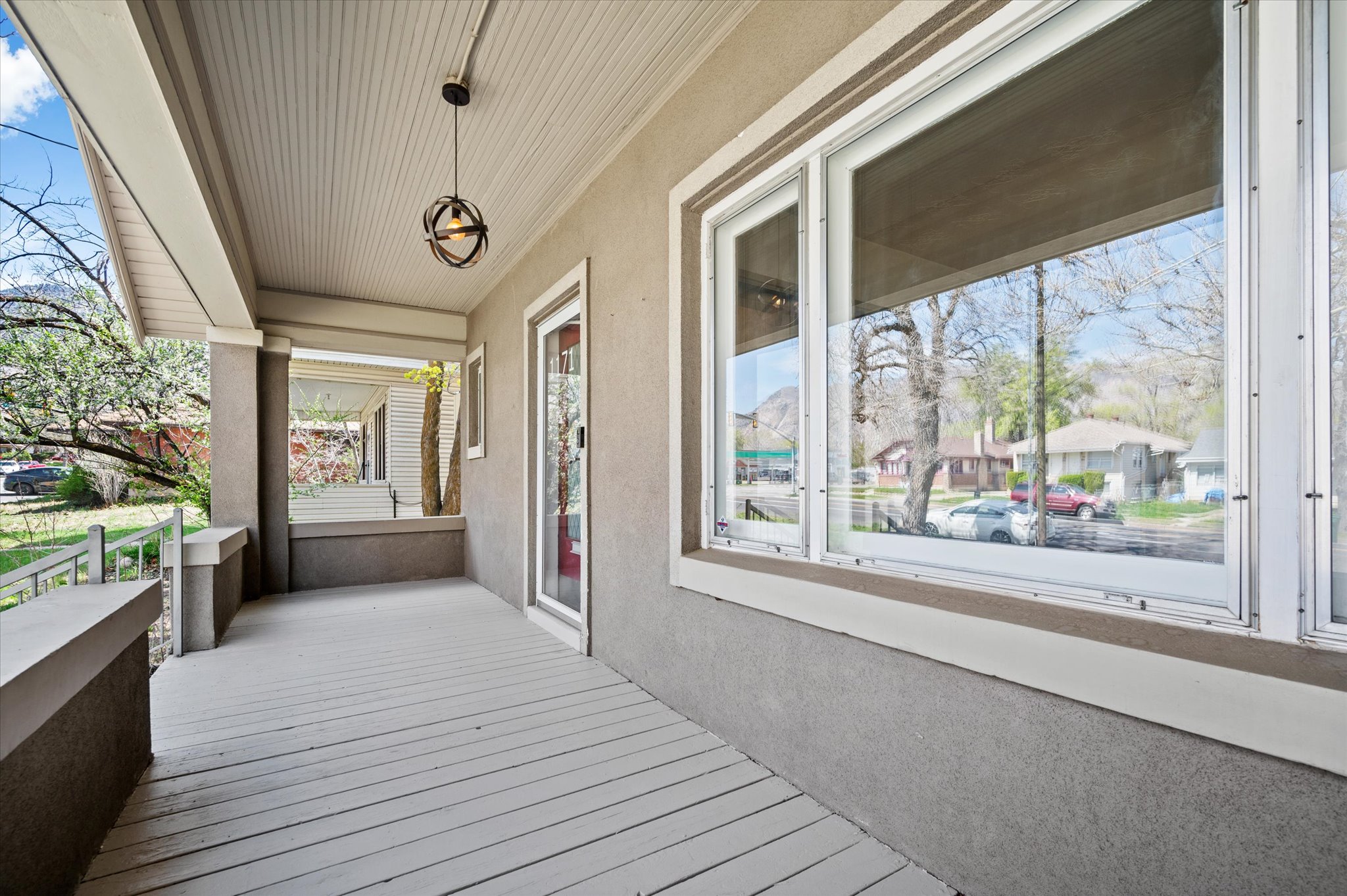 Expansive covered front porch featuring a beadboard ceiling, orb pendant light fixture, and large picture windows
