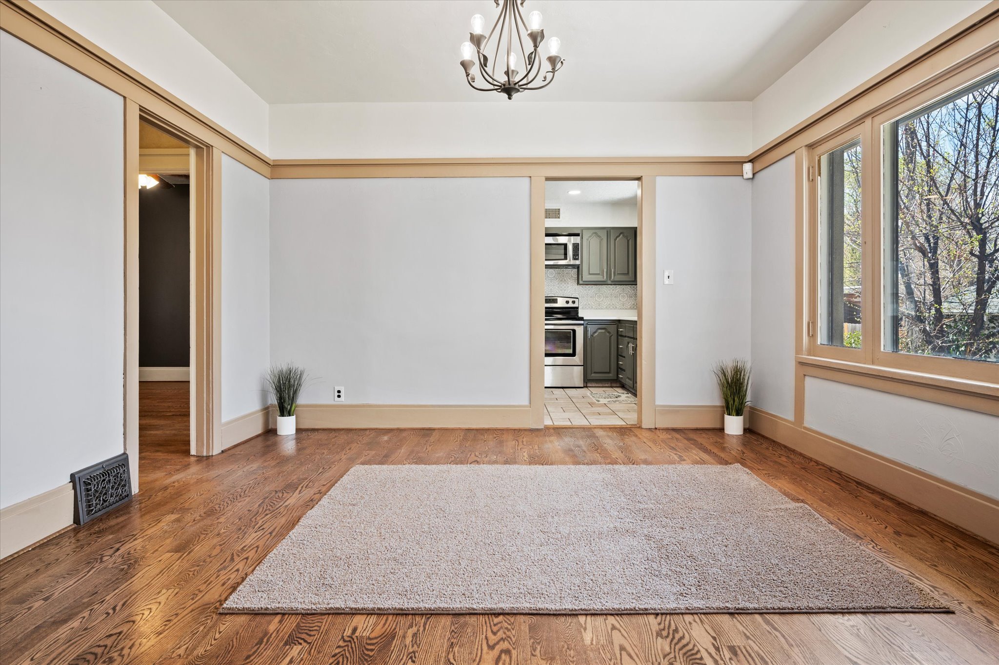 Spacious room featuring rich wood-finish flooring, ample natural light from large windows, and an elegant chandelier