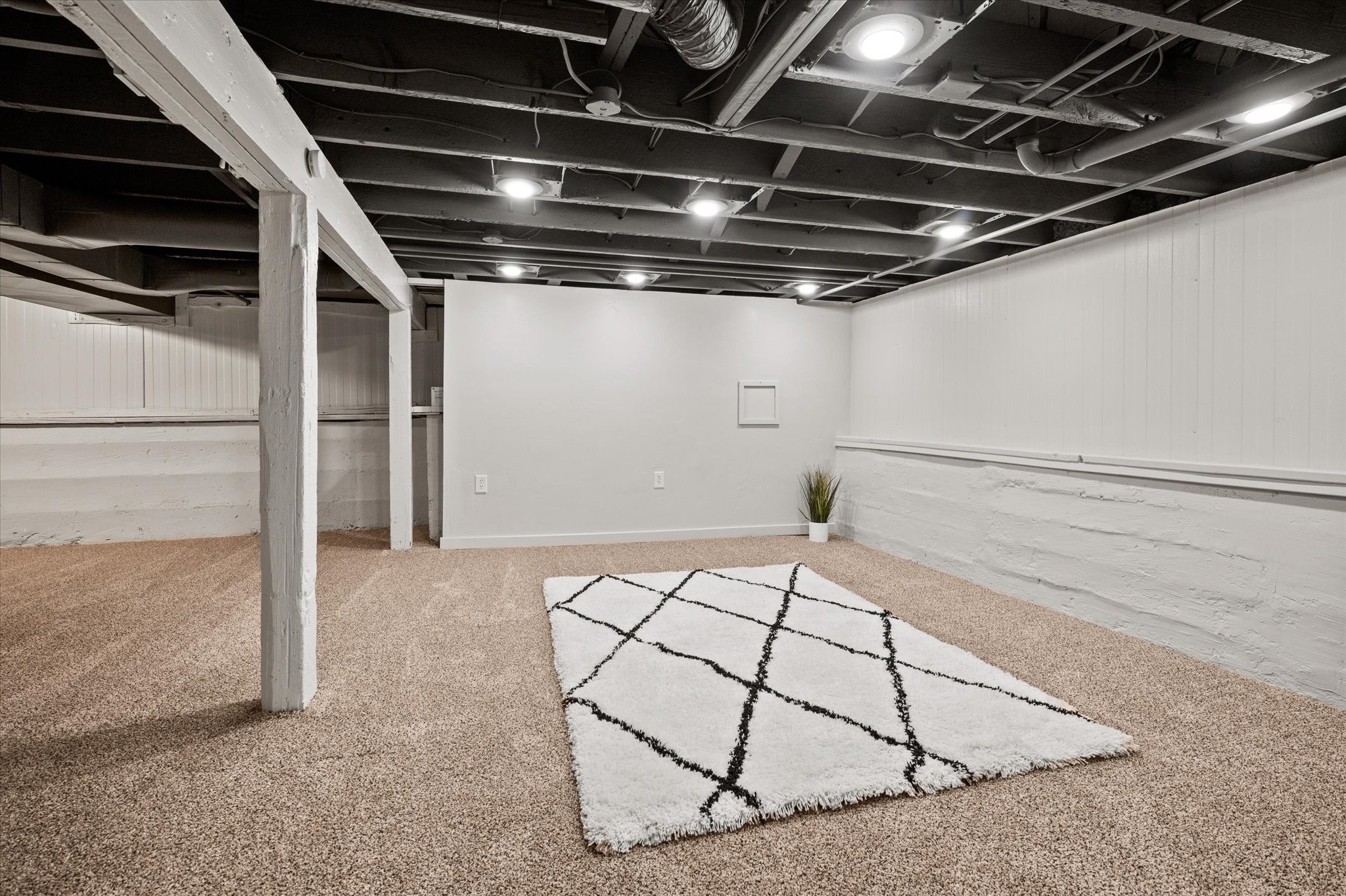 Expansive basement featuring exposed ceiling joists, recessed lighting, carpeted flooring, and painted paneled walls