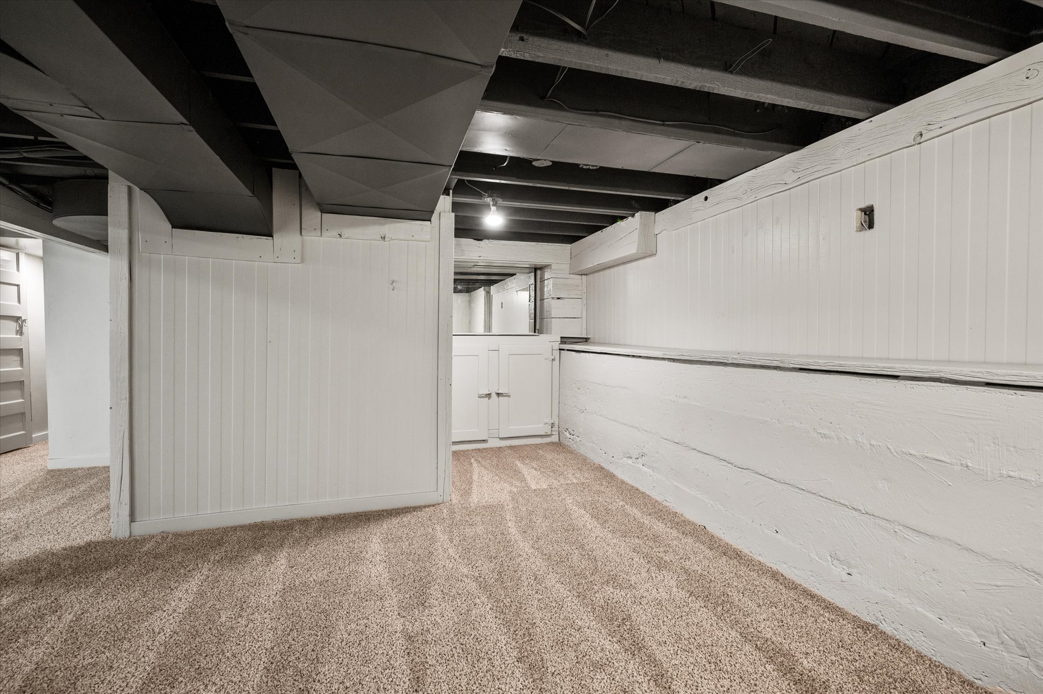 Finished lower level featuring neutral carpet, painted paneling, exposed ceiling joists, and ductwork