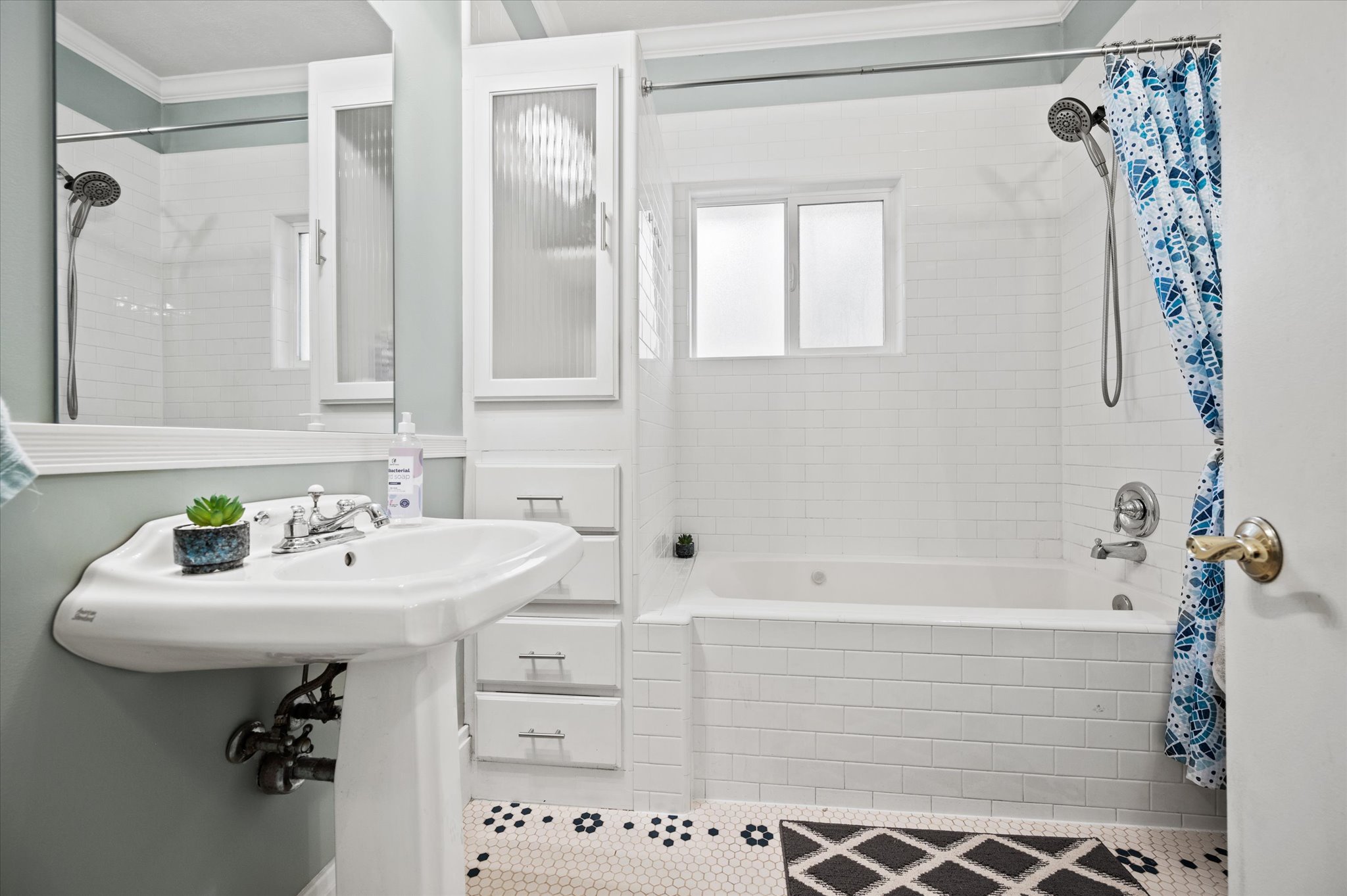 Bathroom featuring a pedestal sink, white subway tile shower surround, built-in cabinetry with reeded glass fronts, and black and white hexagon tile flooring
