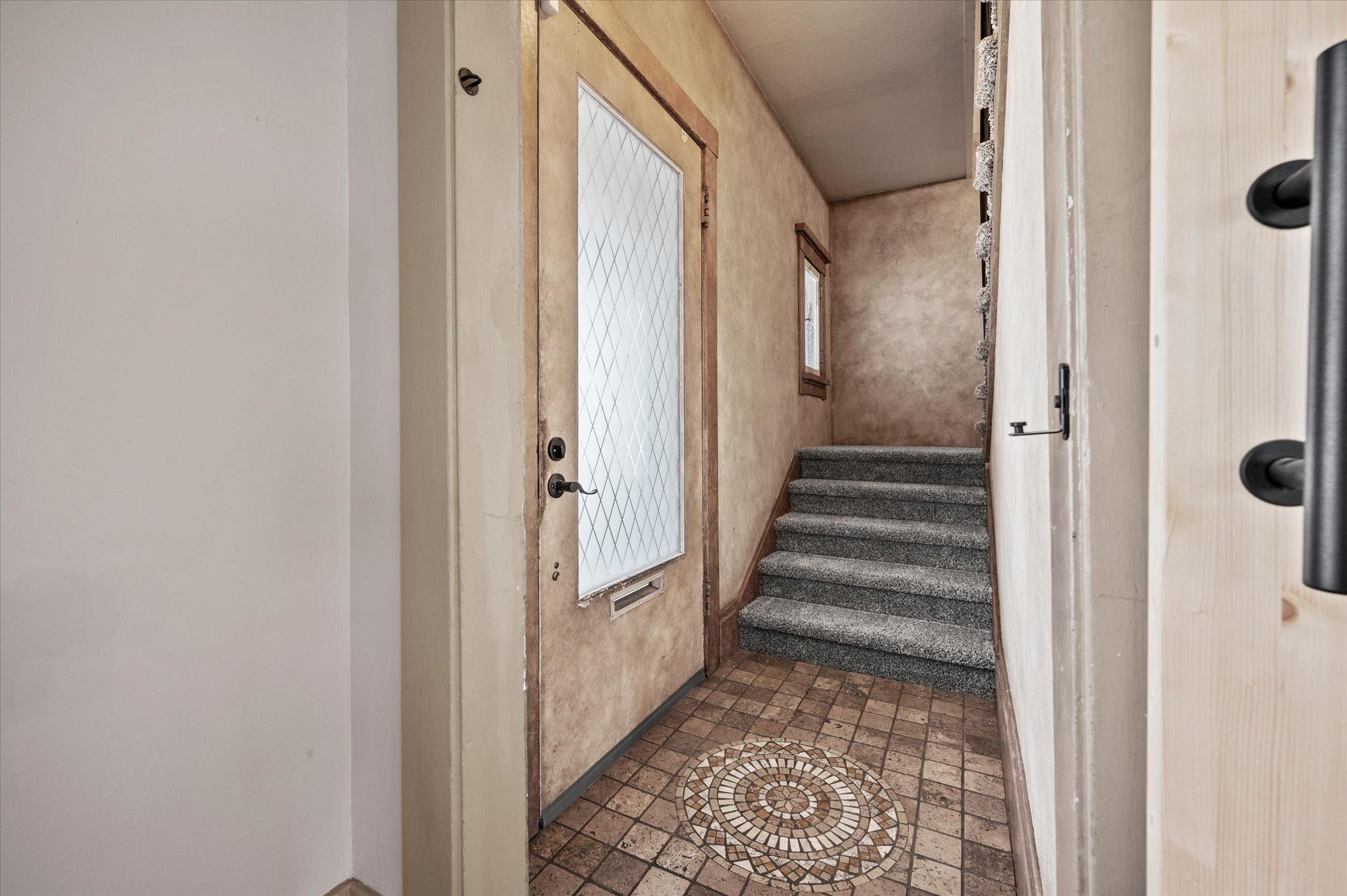Entryway featuring a decorative mosaic tile floor, a front door with a diamond-patterned glass insert, and a carpeted staircase leading upwards
