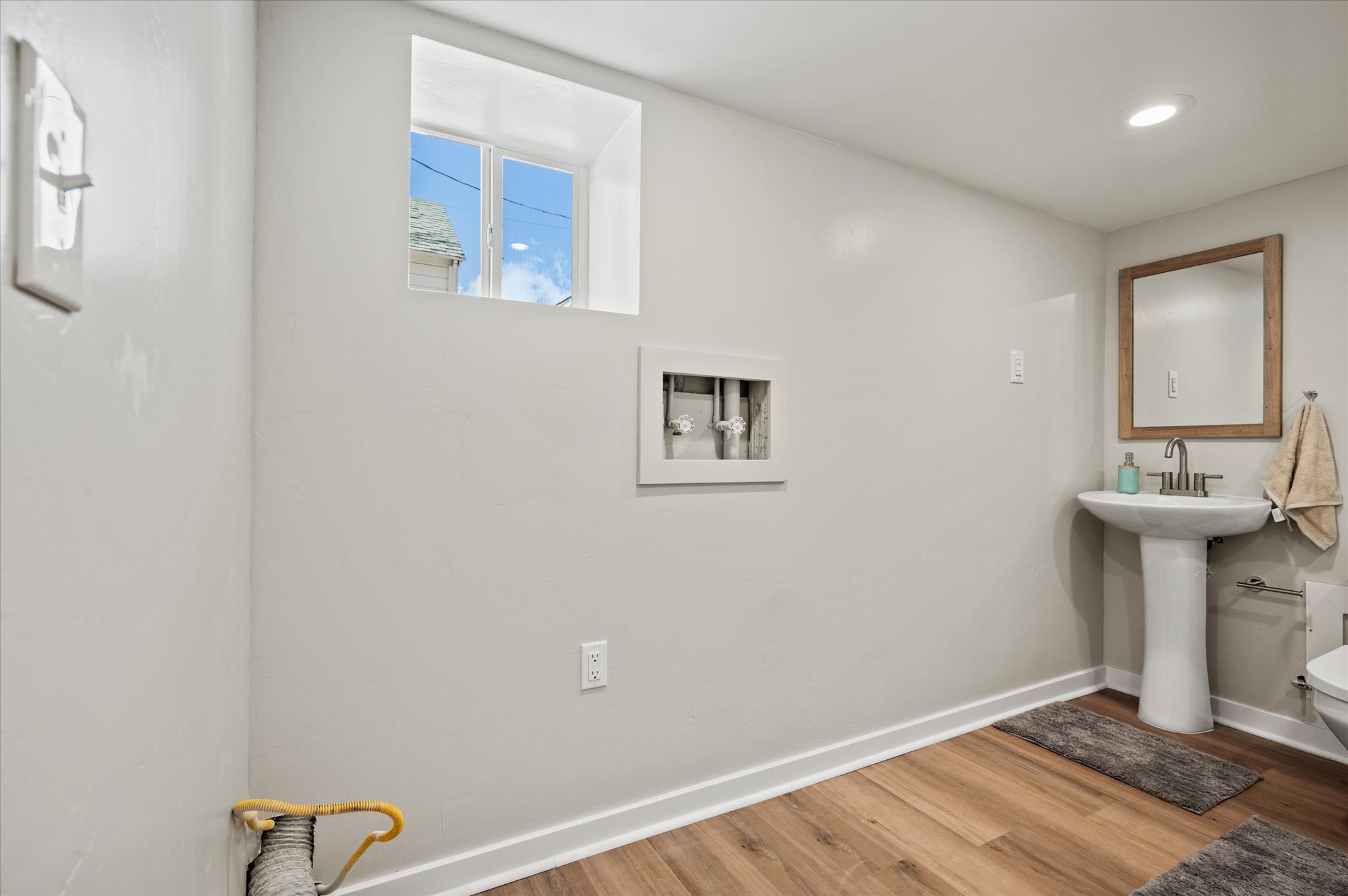 Pedestal sink with a framed mirror, recessed lighting, and wood-finish flooring