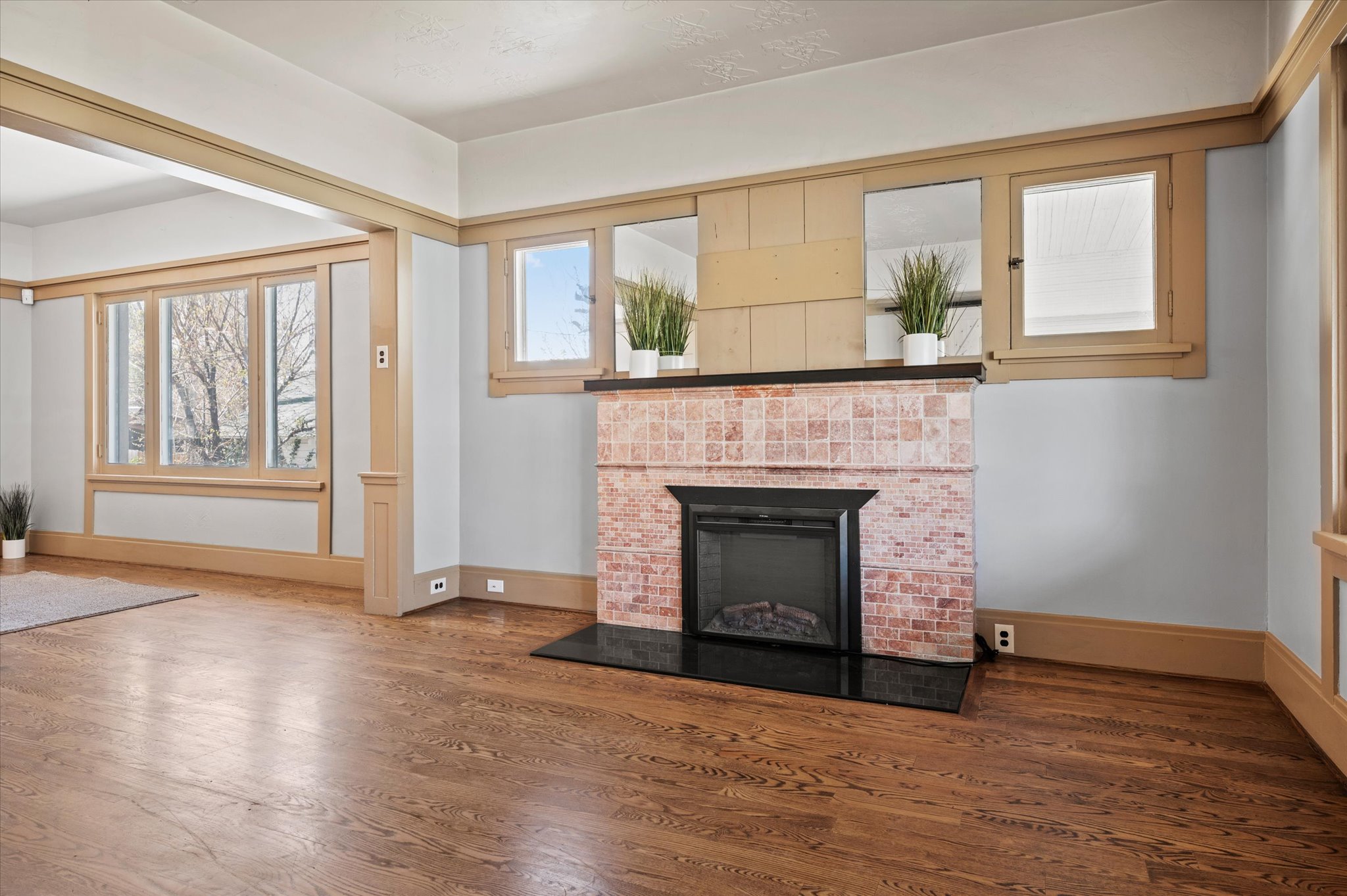 Living area featuring wood-finish flooring, a tiled fireplace with a black hearth, extensive wood trim, multiple windows, and a cased opening