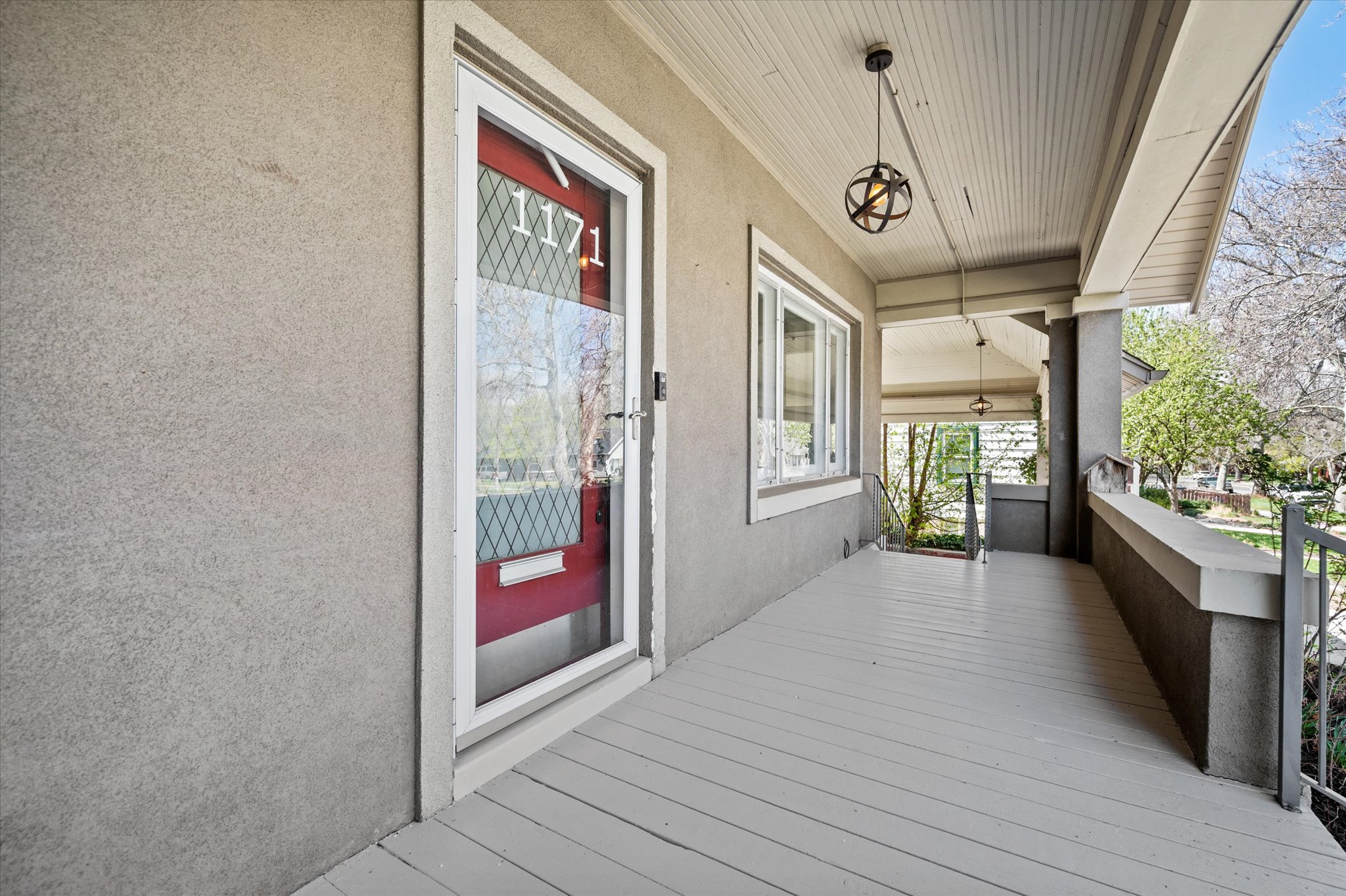 Front porch with painted wood-finish flooring, stucco exterior, and a red entry door with a storm door