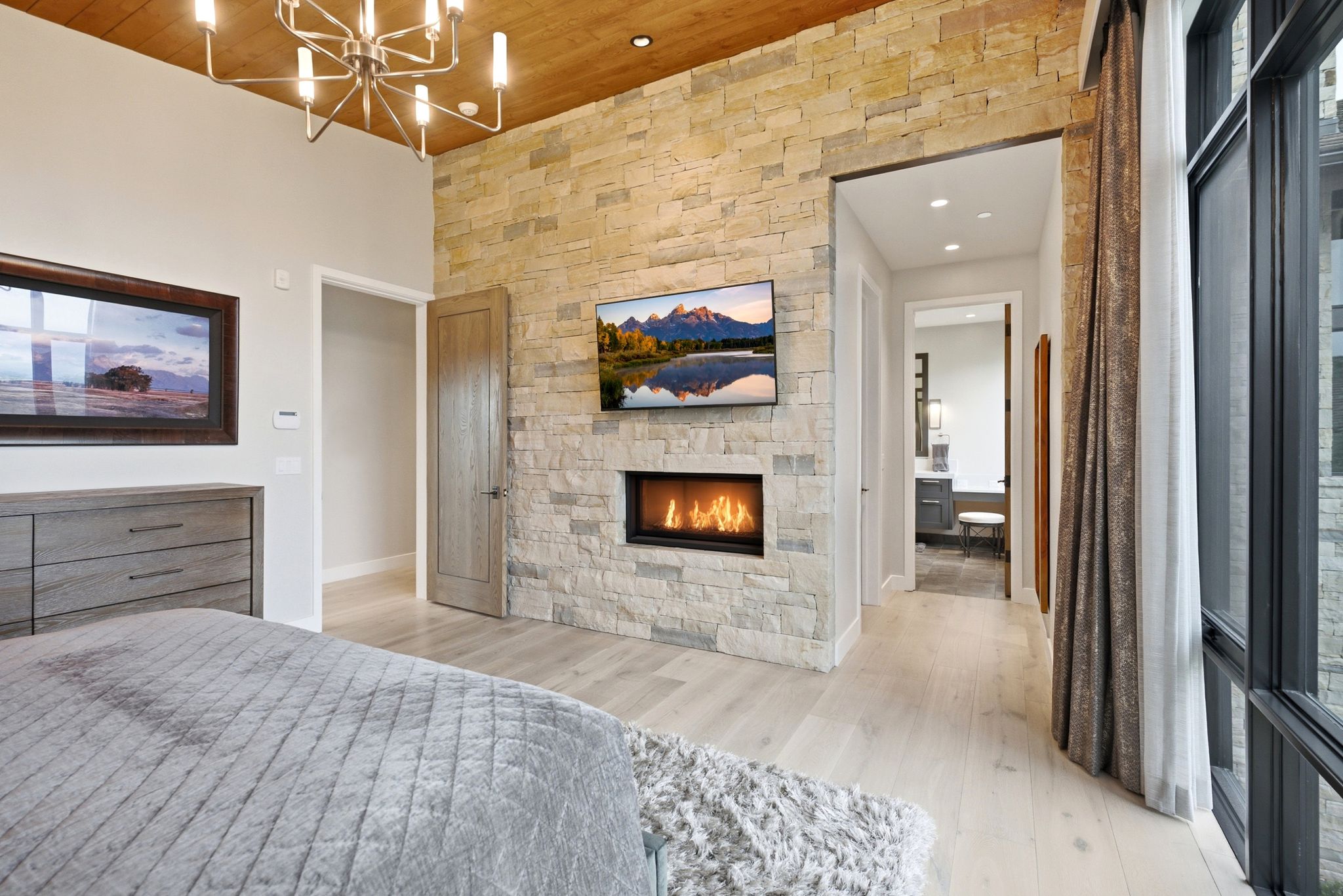 Accent stone wall featuring a linear gas fireplace and mounted television