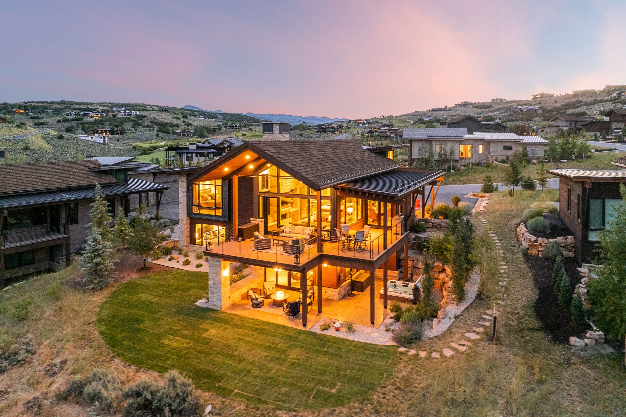 Contemporary architecture featuring extensive glass facades, a prominent covered deck, a lower-level patio, and a stone-clad exterior