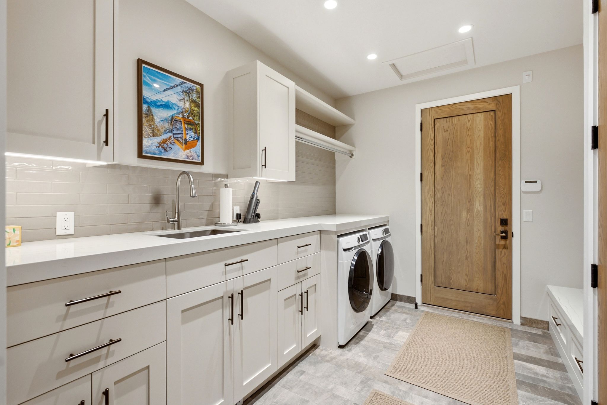 Dedicated laundry room featuring light gray cabinetry, a white countertop with an undermount sink, and a horizontal subway tile backsplash