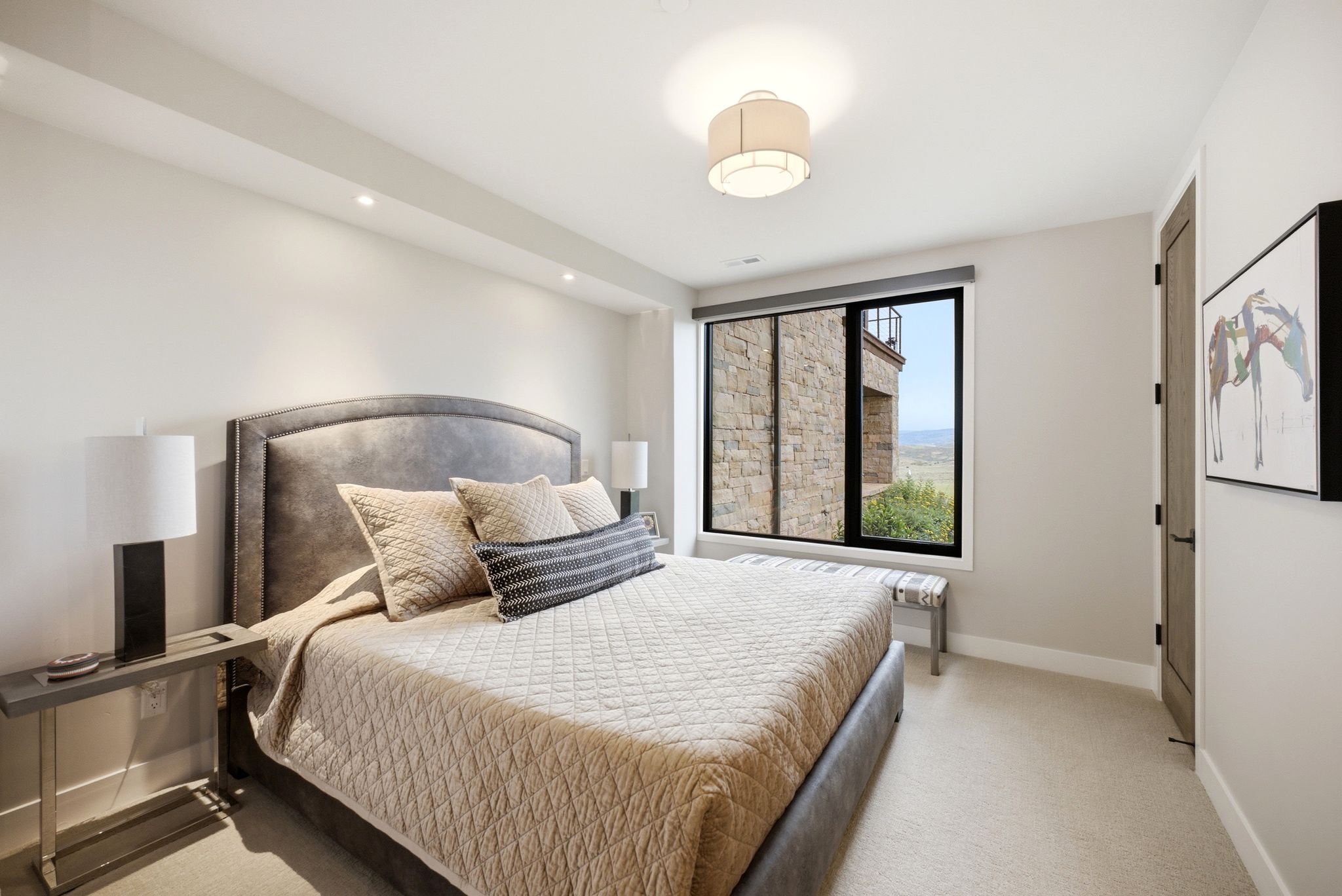Room featuring a large window, a fabric upholstered headboard, recessed ceiling lighting, a contemporary ceiling fixture, and a solid core interior door