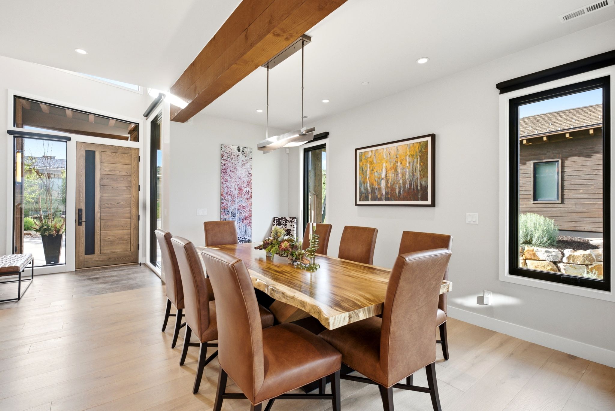 Spacious interior with light wood-finish flooring, a contemporary entryway door with vertical glass paneling, and an exposed wood beam ceiling detail