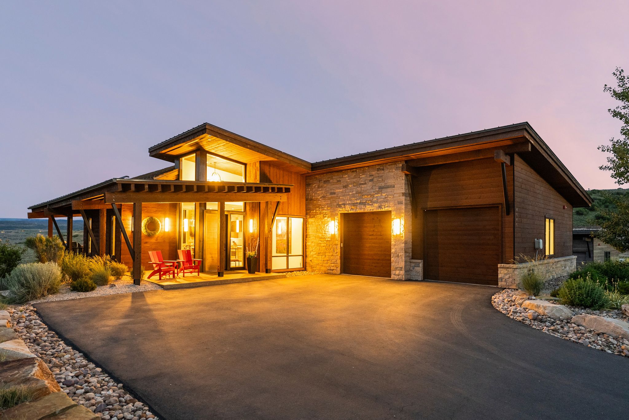 Contemporary architecture featuring wood siding, stone veneer accents, an attached garage, a covered front porch with a wood pergola, and a paved driveway