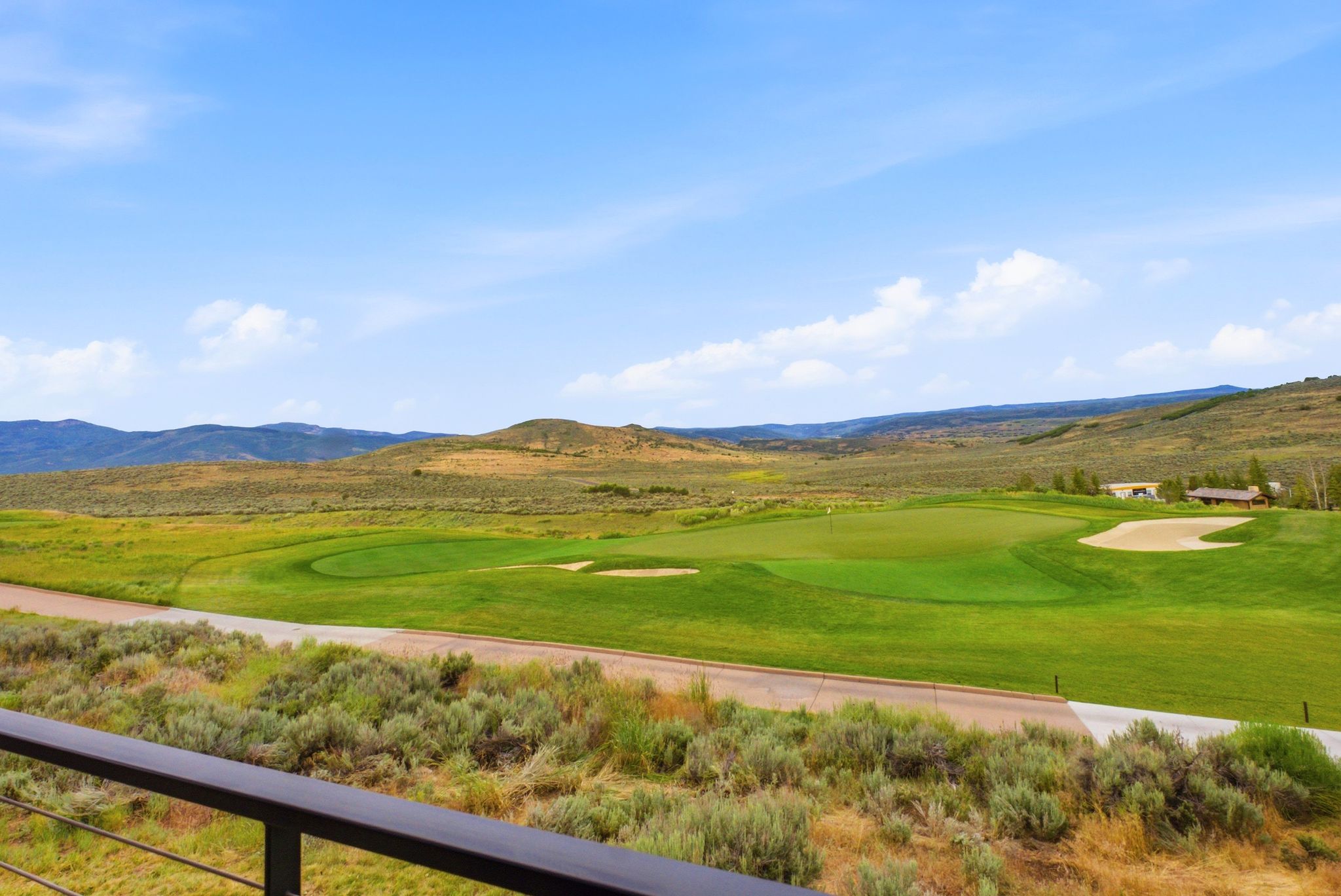 Expansive golf course frontage featuring a putting green and sand bunkers, set against a backdrop of rolling hills and distant mountains