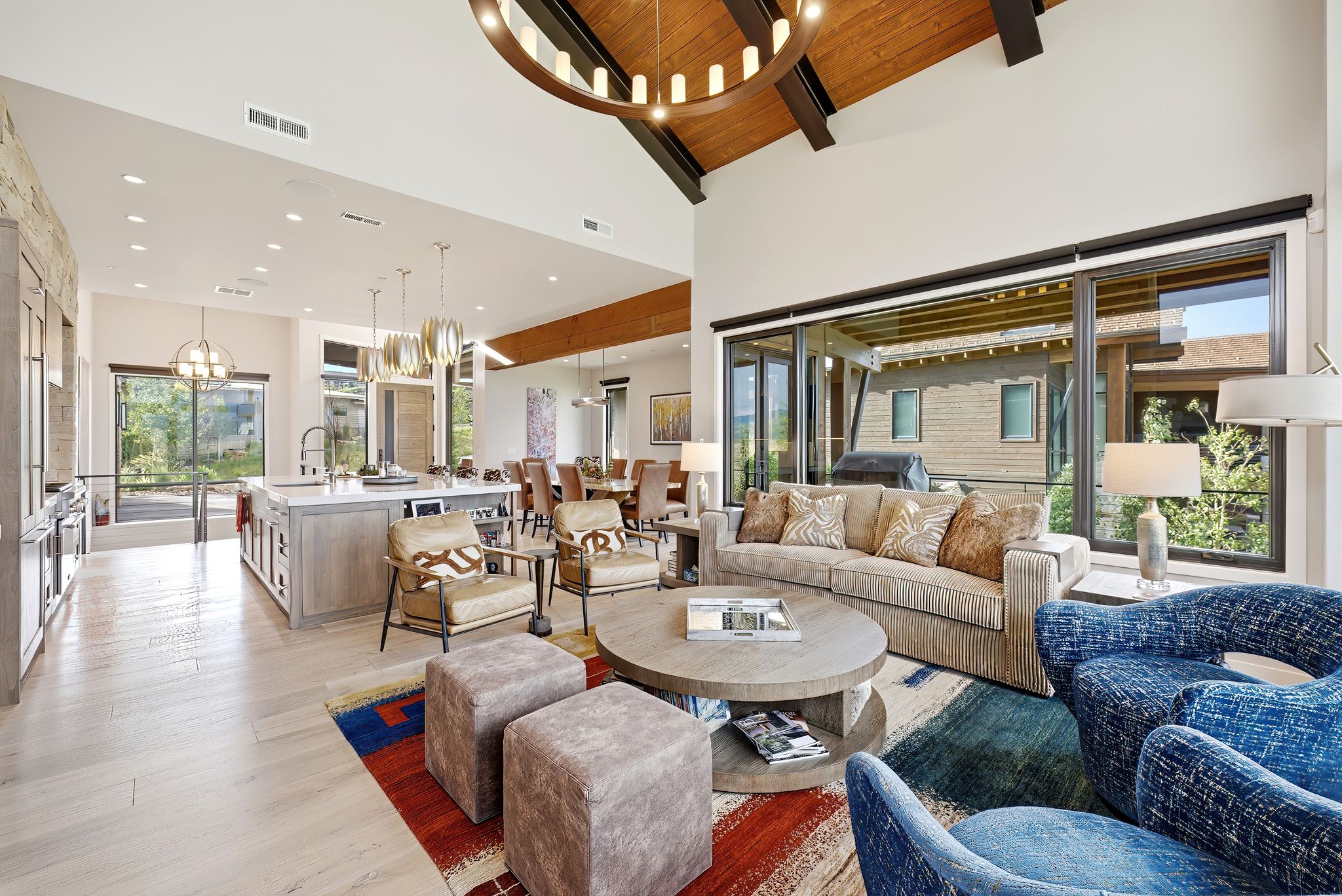 Spacious open-concept living area featuring high vaulted ceilings with exposed wood beams, light wood-finish flooring, and a large sliding glass door