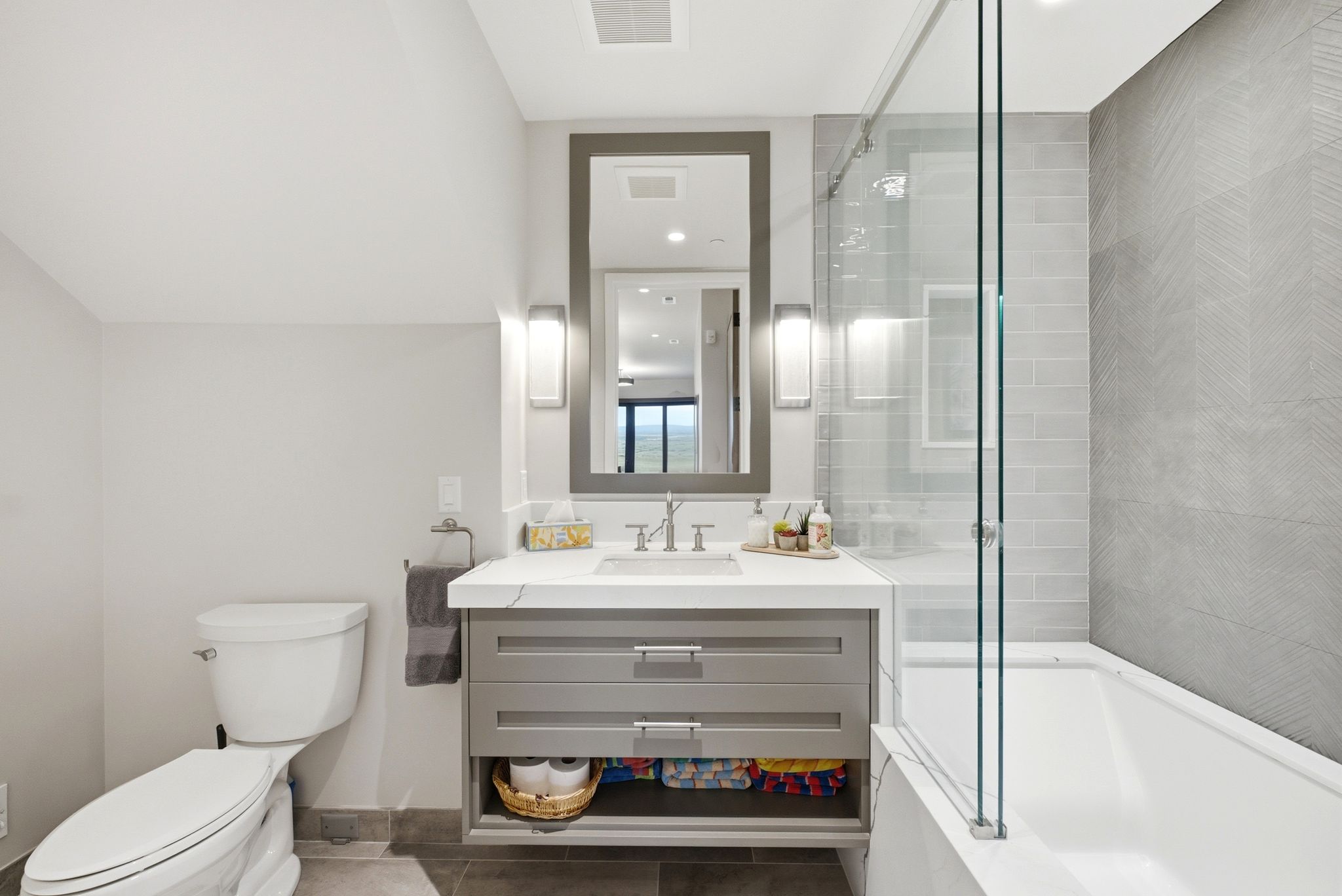 Bathroom featuring a single vanity with a white countertop and rectangular undermount sink, gray cabinetry, and a framed mirror with sconce lighting