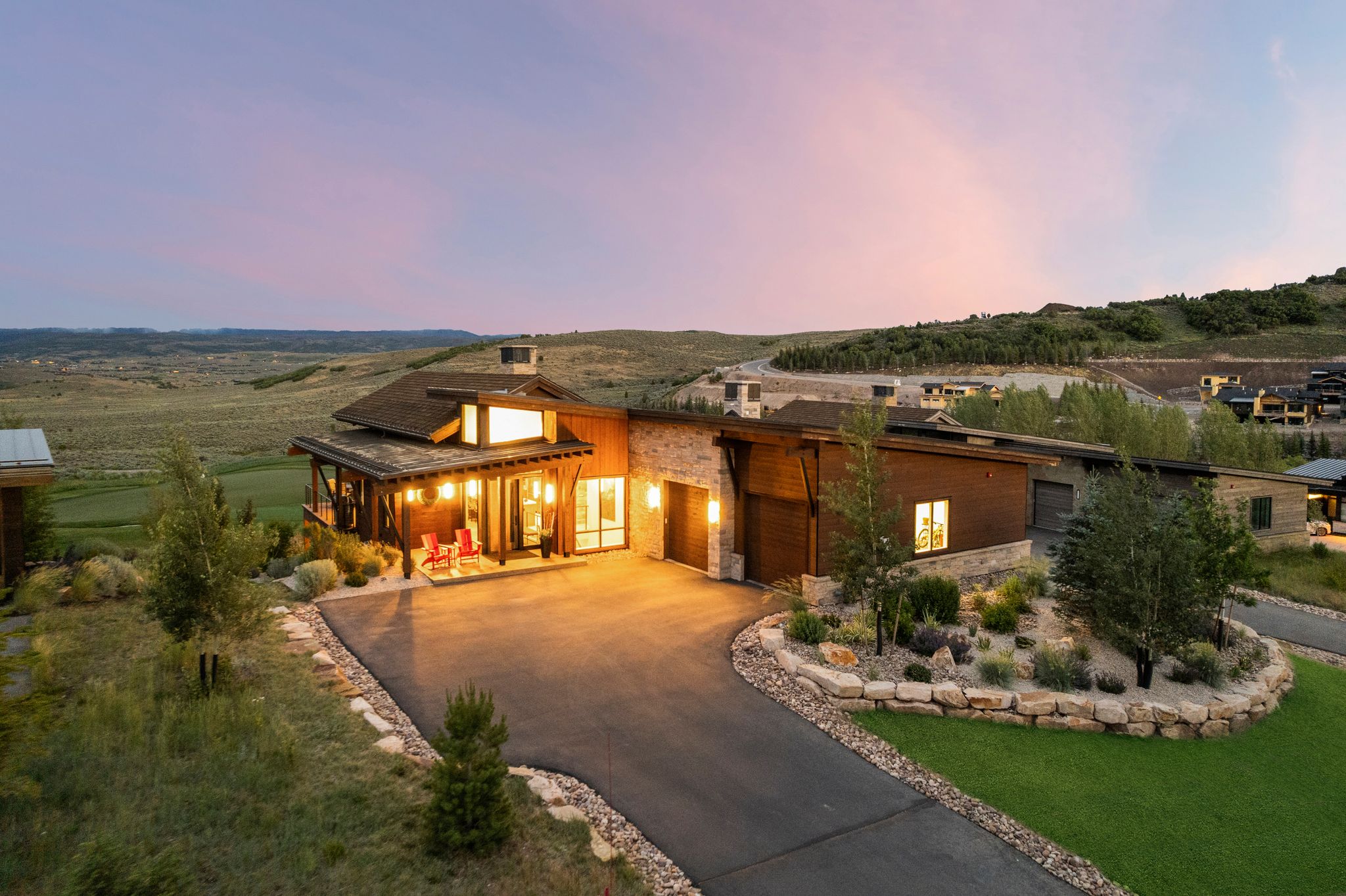 Contemporary architectural design featuring a spacious driveway, stone veneer accents, wood siding, a covered porch, and extensive landscaping