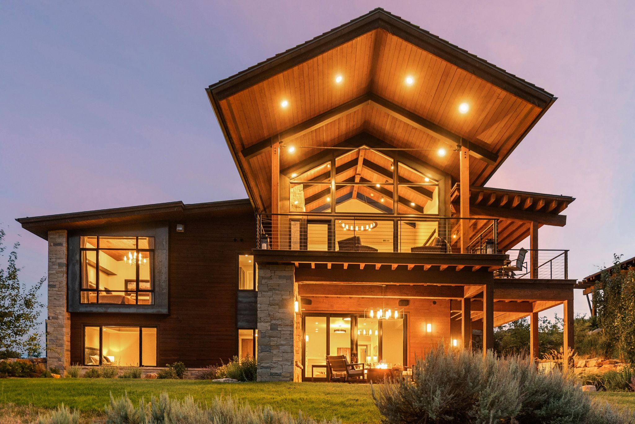 Contemporary multi-level residence featuring expansive windows, wood-clad ceilings, a large upper-level balcony, a lower-level patio, and stone accents