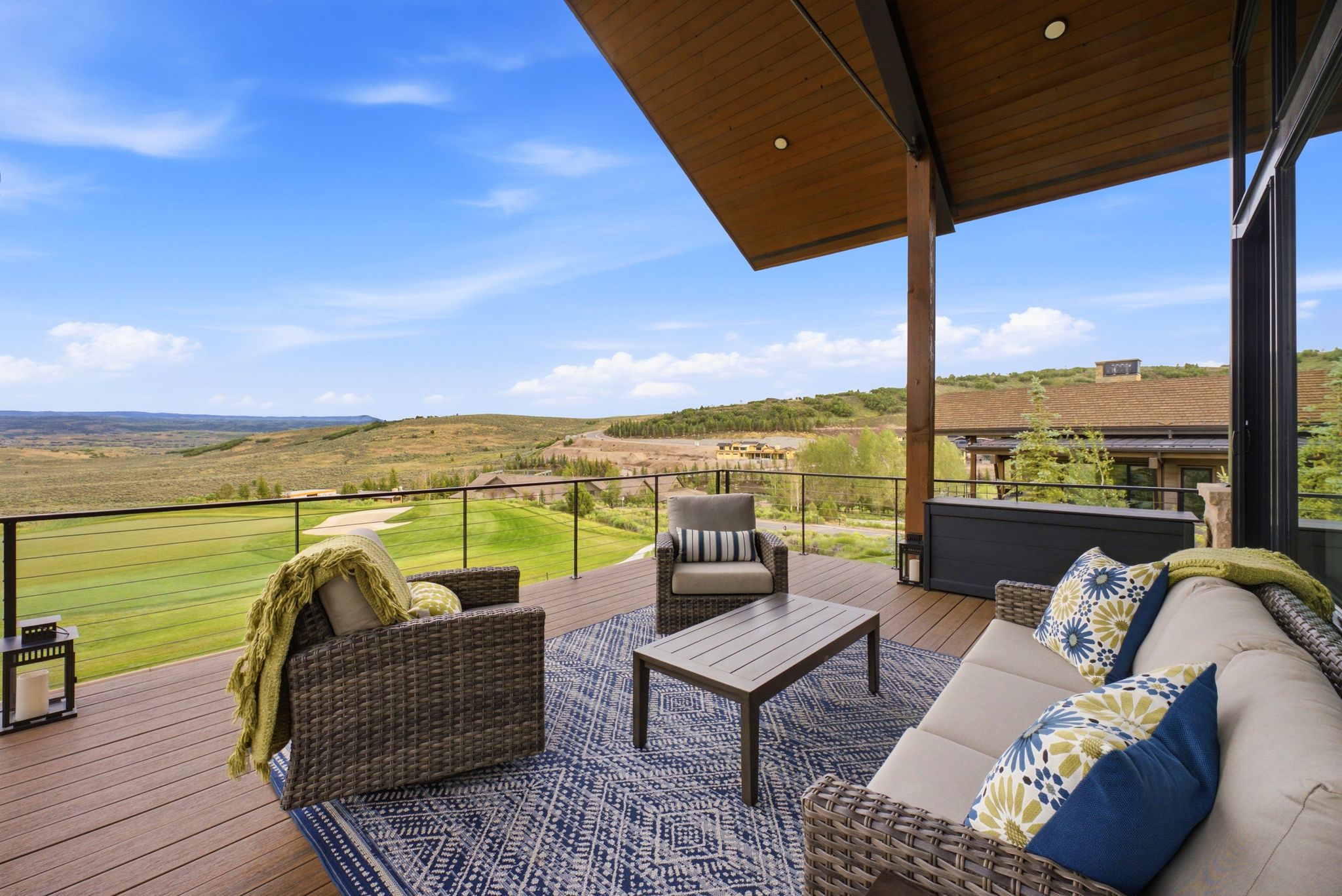 Spacious outdoor deck featuring wood-finish flooring, a metal and glass railing system, and an expansive covered patio area