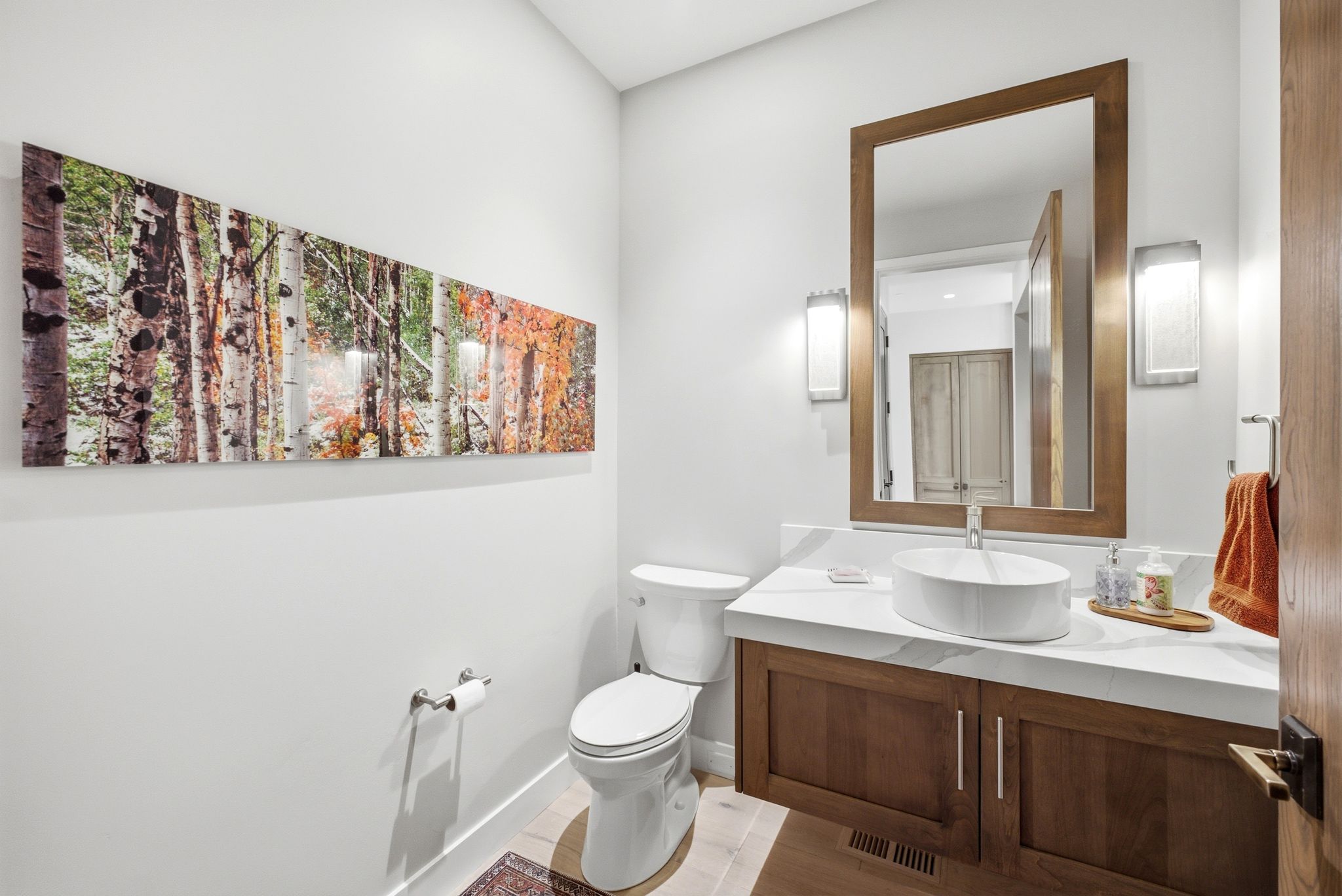 Floating wood-finish vanity with a vessel sink, white countertop, and prominent wood-framed mirror