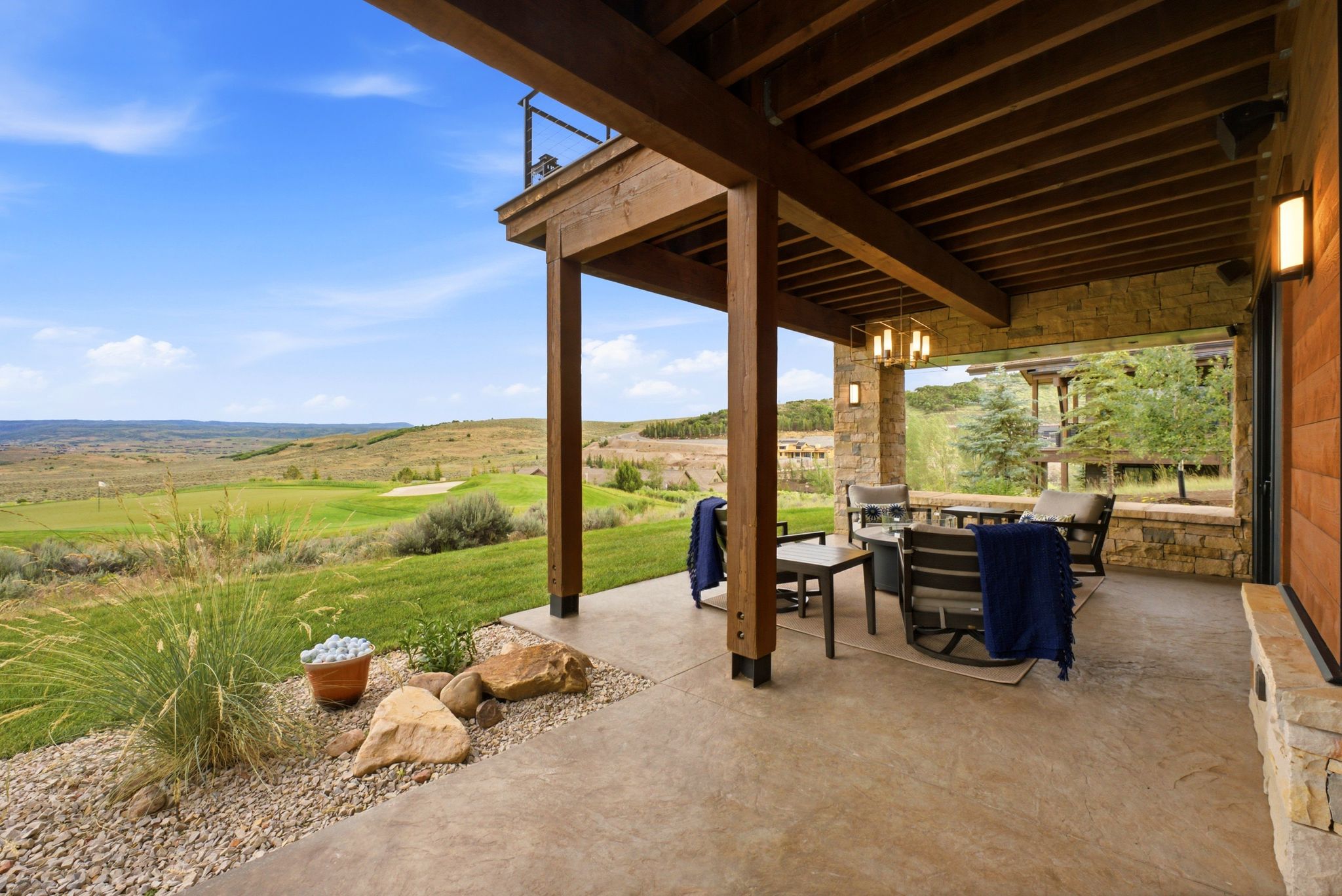 Covered patio featuring a wood-beam ceiling, stone accent walls, and concrete flooring