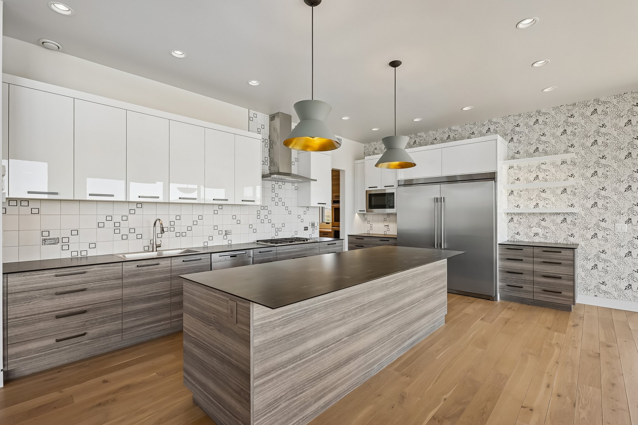 Kitchen featuring a large island, wood-finish flooring, two pendant light fixtures, white upper cabinetry, and stainless steel appliances