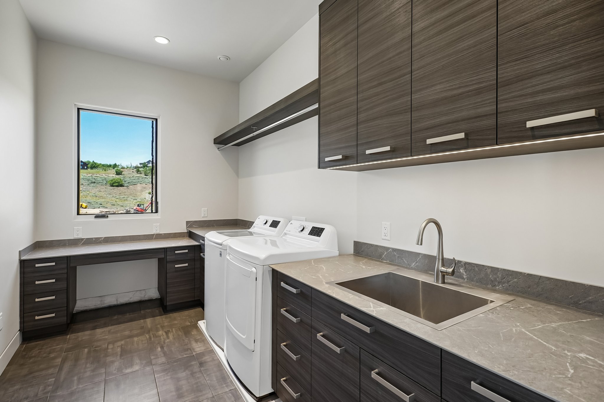 Dedicated laundry room featuring wood-finish cabinetry, stone-look countertops, and a built-in stainless steel sink