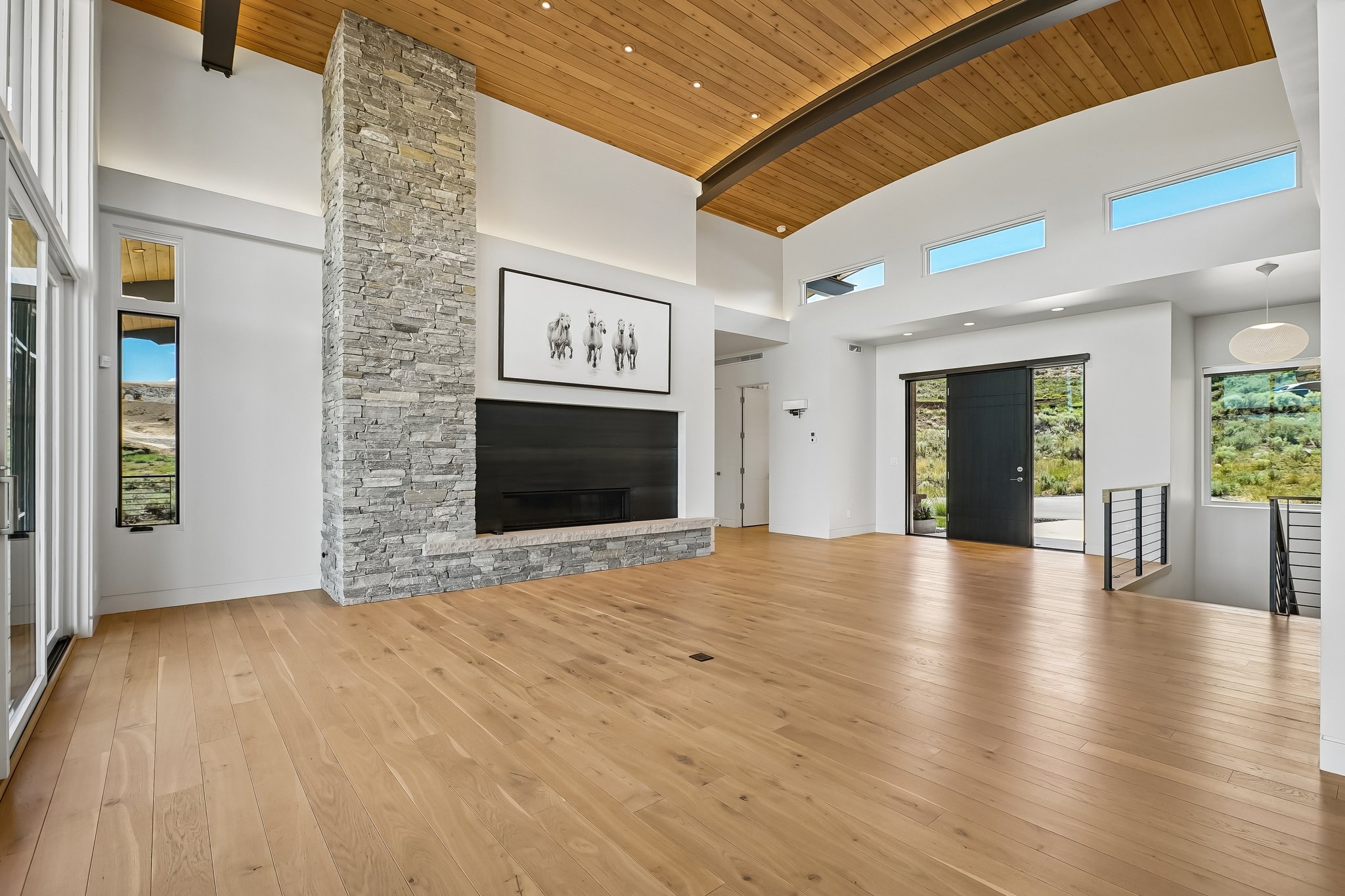 Spacious room featuring light wood-finish flooring, a floor-to-ceiling stone fireplace, and a wood-paneled ceiling with exposed beams