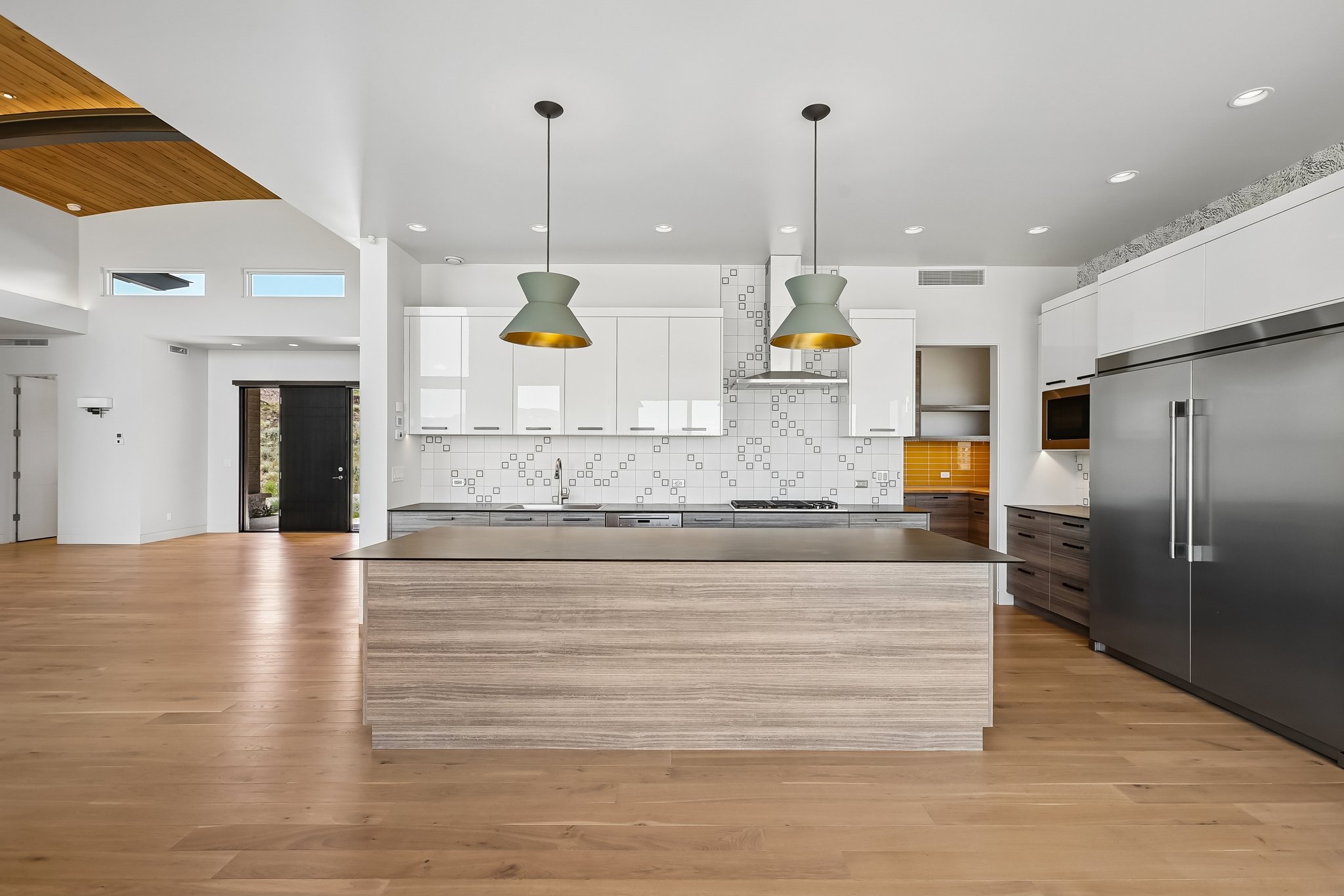 Modern kitchen featuring a wood-finish island with a dark countertop, white upper cabinetry, stainless steel appliances, and a patterned tile backsplash