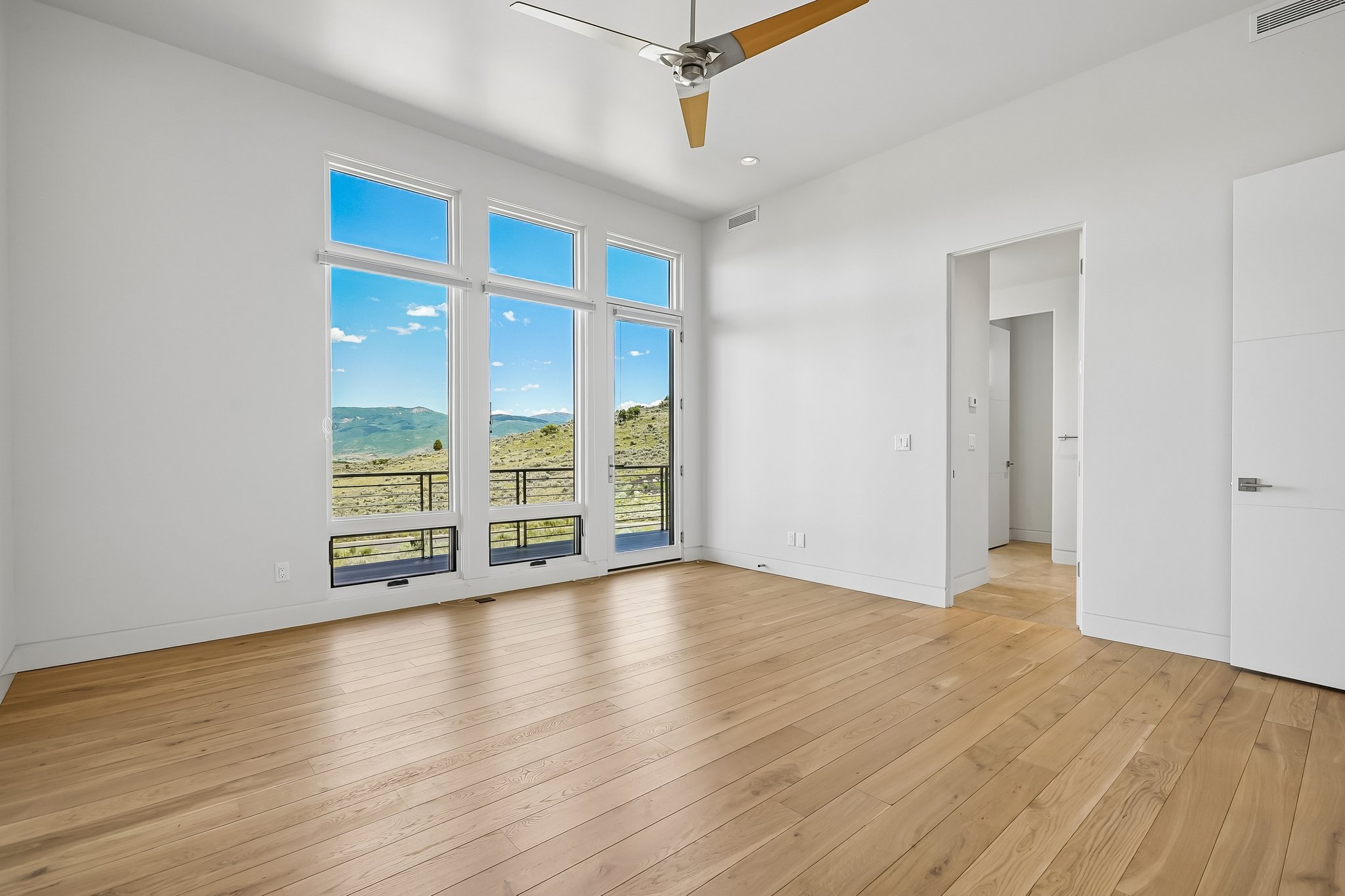 Expansive room featuring multiple full-height windows, light wood-finish flooring, and a contemporary ceiling fan
