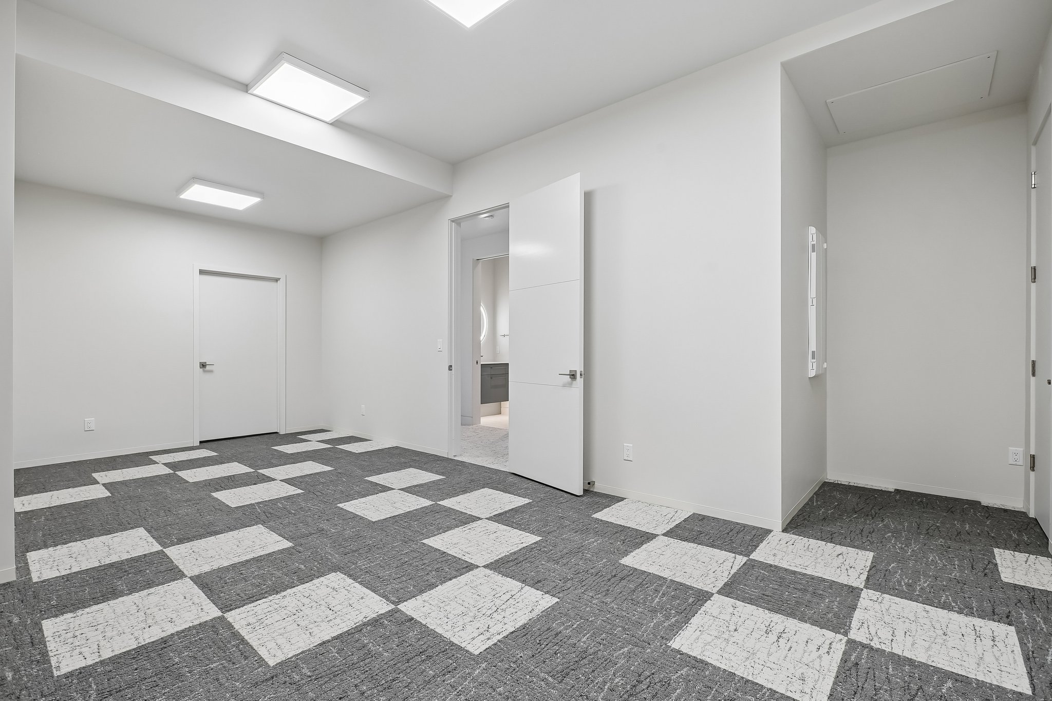 Spacious room featuring geometric pattern carpeting, contemporary white walls, modern flush-mount lighting, and white interior doors