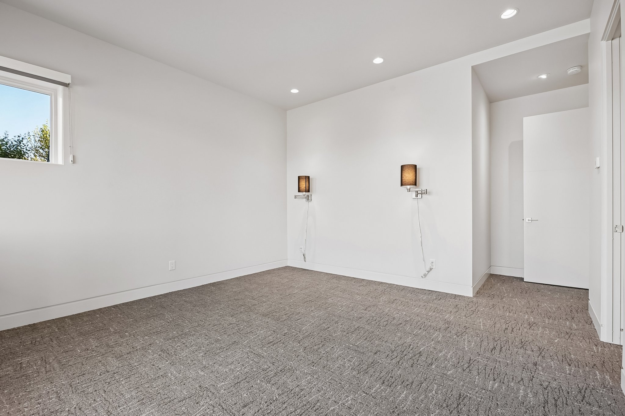 Bright room featuring recessed lighting, a modern window, two wall-mounted sconces, and neutral-toned patterned carpeting
