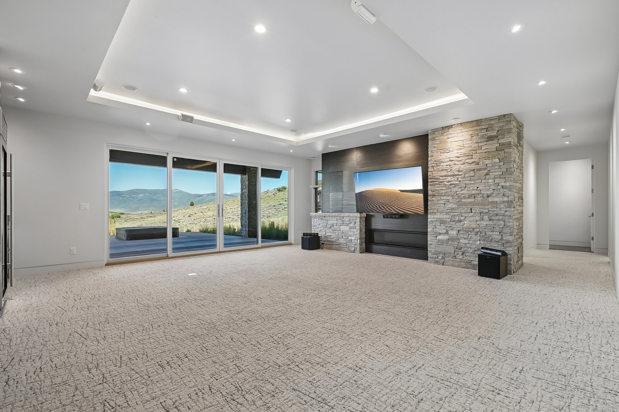 Spacious room featuring broad sliding glass doors, a stone veneer accent wall, recessed lighting, a tray ceiling with integrated lighting, and carpeted flooring