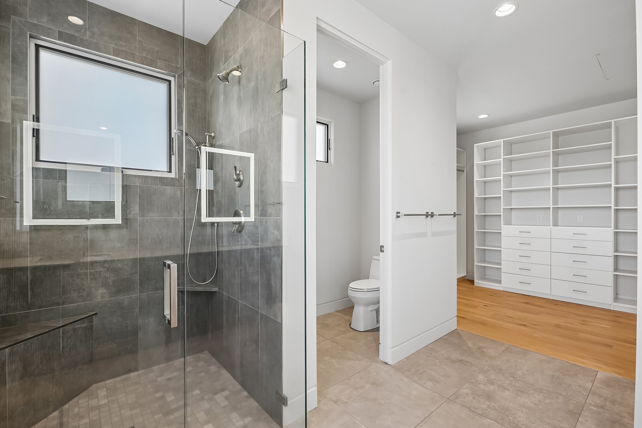 Walk-in shower with full glass enclosure, two-tone tile surround, built-in bench, and dual shower heads