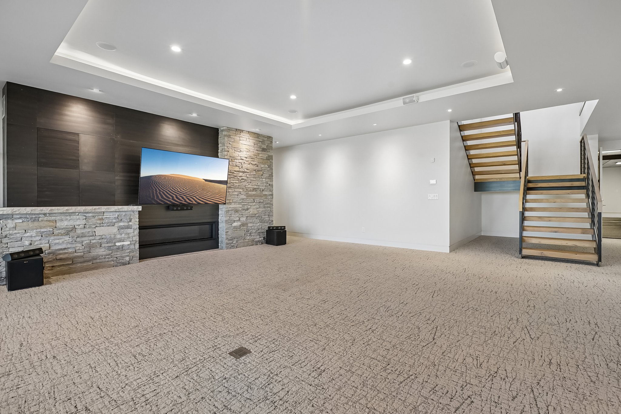 Spacious entertainment area featuring a contemporary fireplace with stone surround, accent wall, recessed lighting, and a floating staircase with wood treads and metal railings