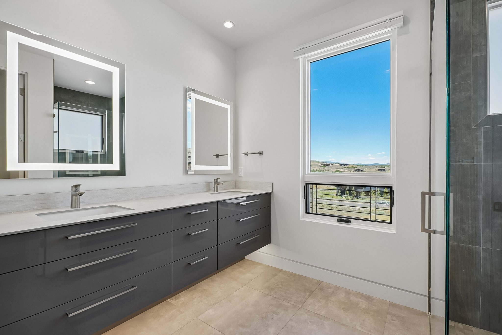 Contemporary bathroom featuring a long double vanity with dark cabinetry and light countertops, dual rectangular undermount sinks, and two illuminated mirrors
