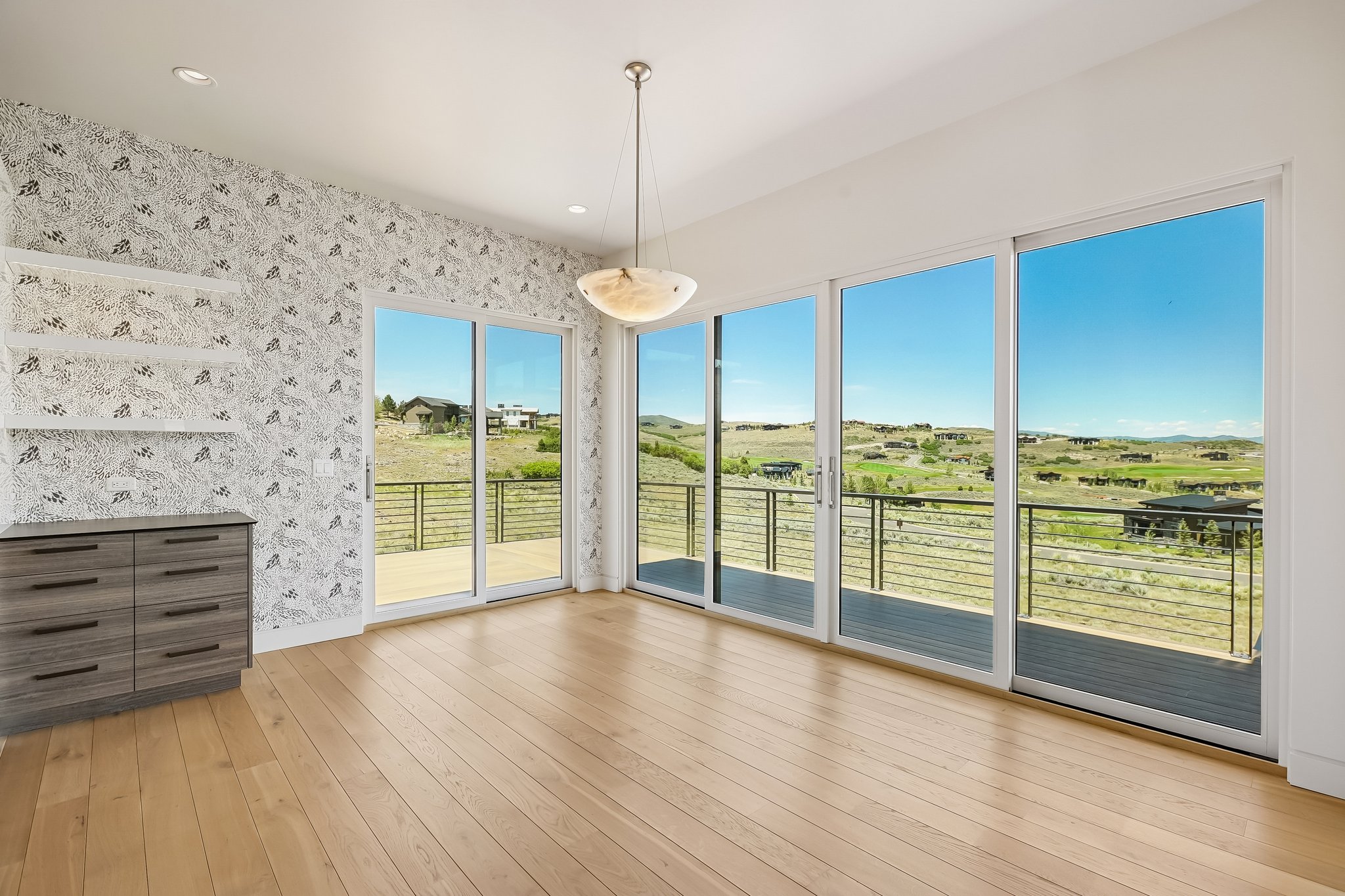 Spacious room featuring light wood-finish flooring and extensive sliding glass doors opening to an outdoor deck with metal railings