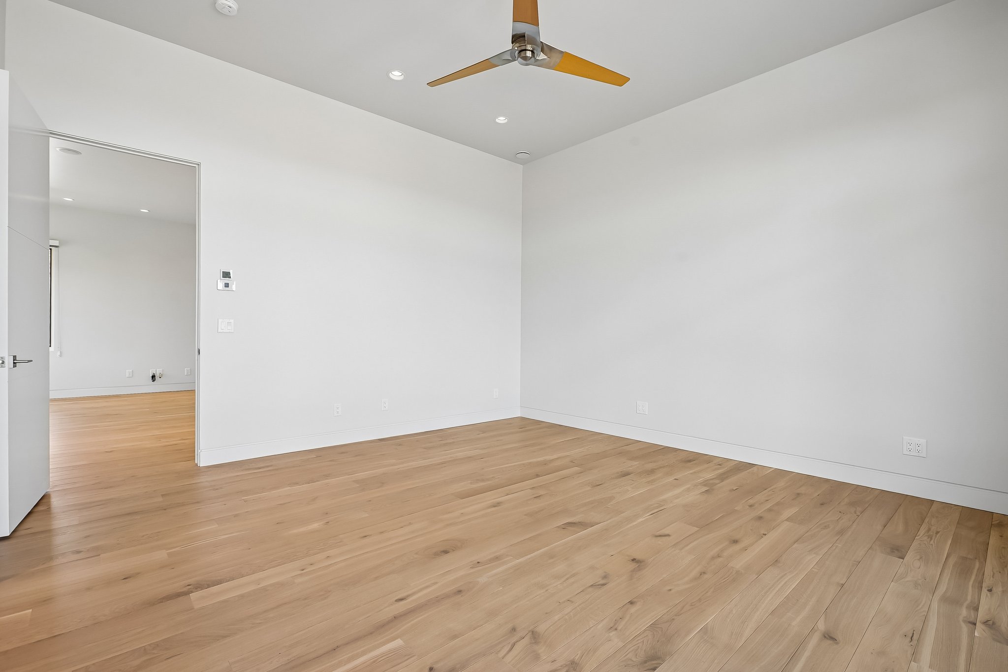 Spacious room featuring light wood-finish flooring, recessed lighting, a modern ceiling fan, and a neutral color palette