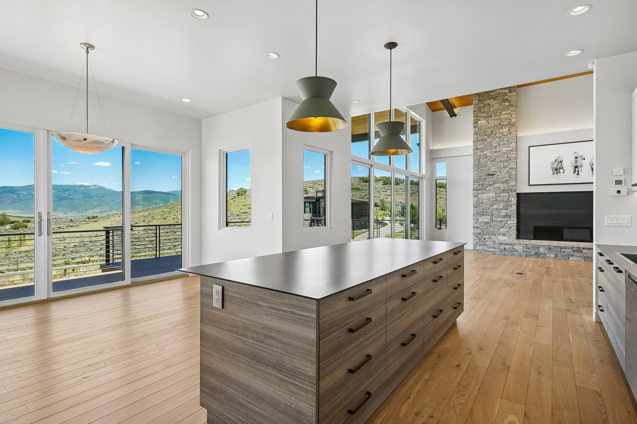 Expansive open-concept room featuring light wood-finish flooring, a large kitchen island with drawers, and a stone-clad fireplace