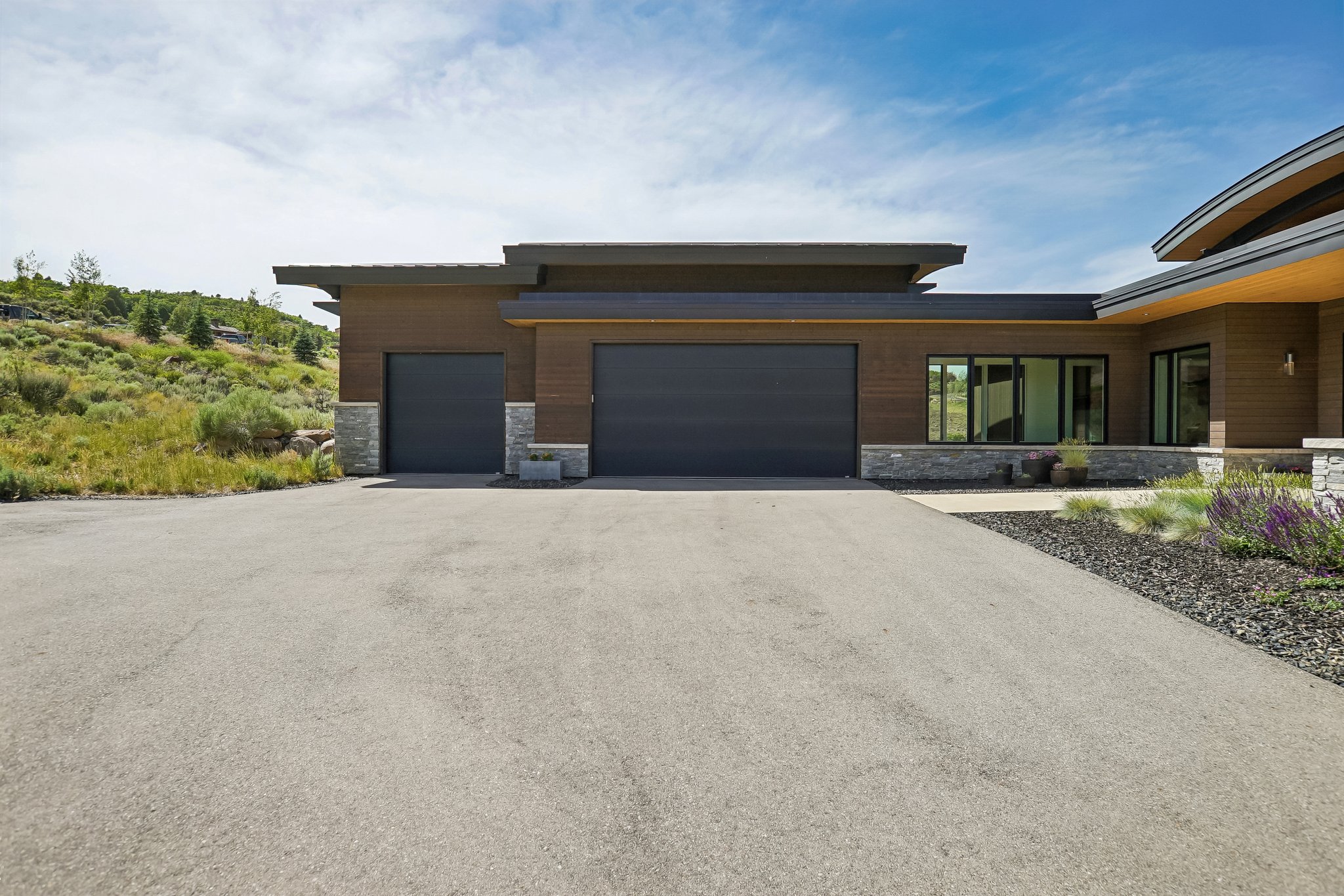 Modern exterior featuring wood-tone siding, stone accents, and multiple garage doors
