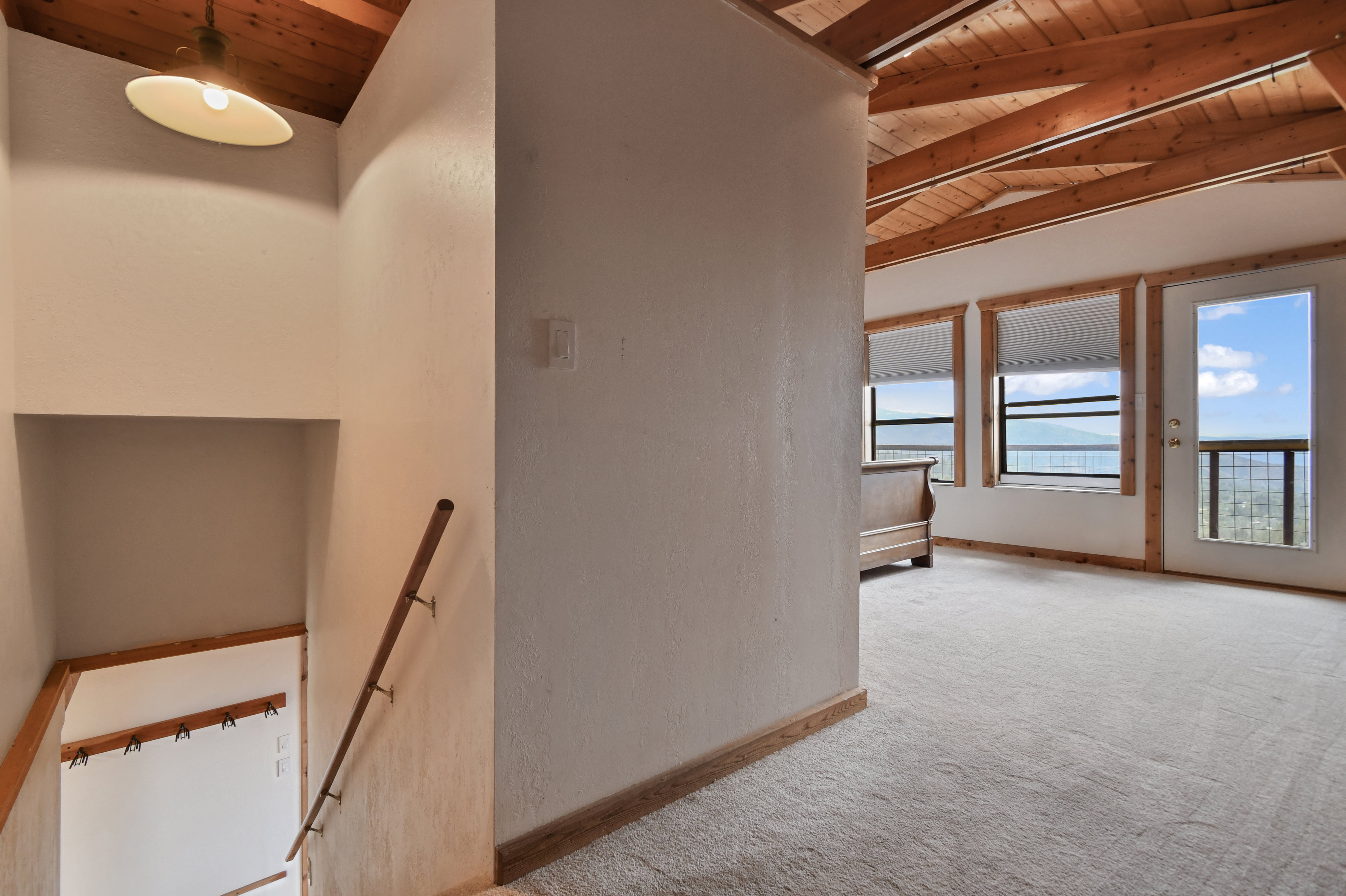 Carpeted room with exposed wood beam ceiling, wood-trimmed windows, and a glass-paneled door