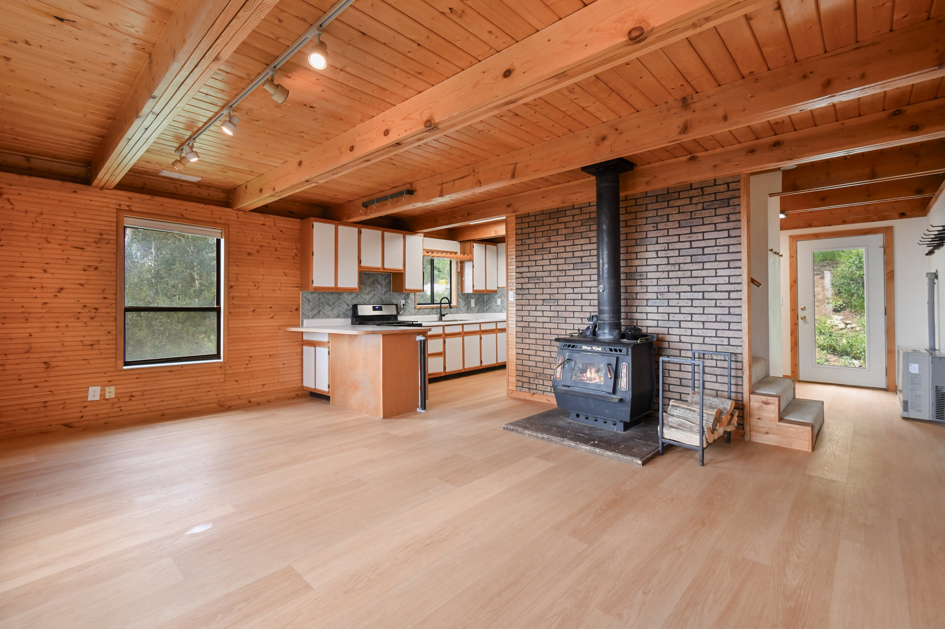 Open-concept living space featuring wood-finish flooring, exposed wood beam ceiling, and horizontal wood paneling