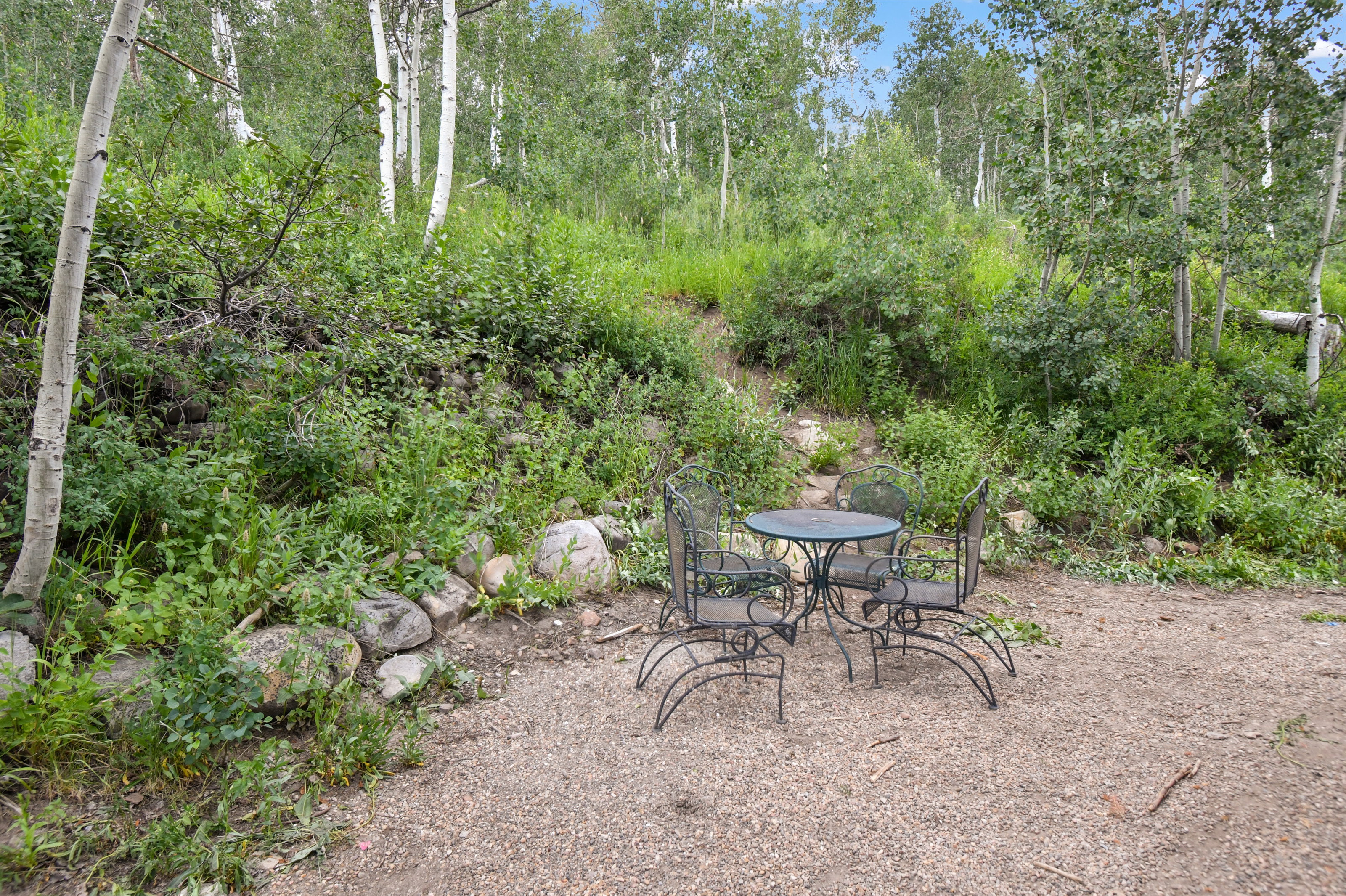 Outdoor gravel patio area surrounded by natural landscaping and mature trees