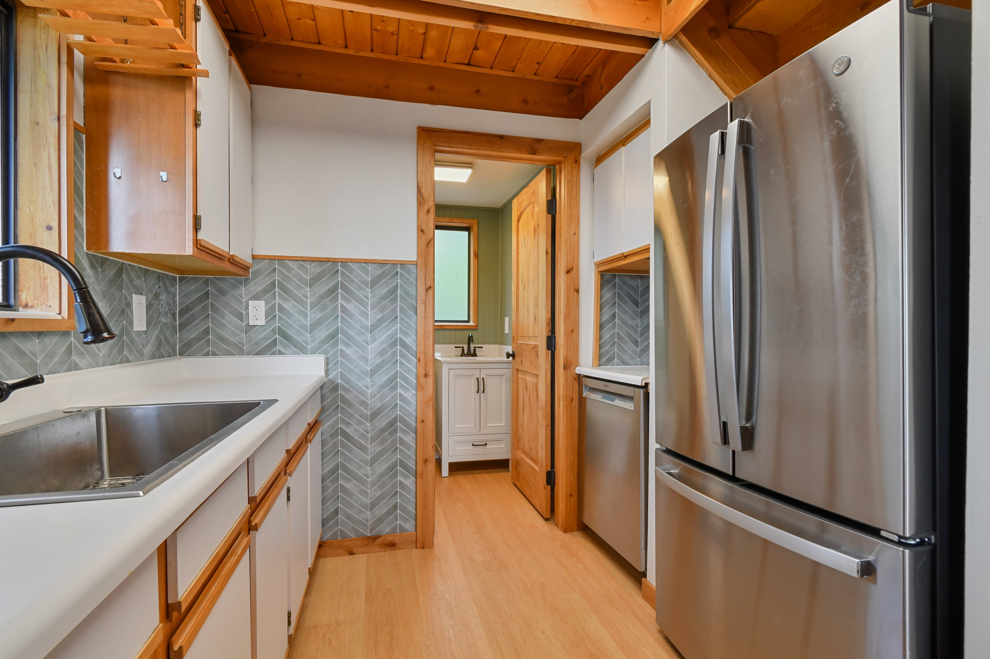 Kitchen featuring wood-finish flooring, stainless steel appliances, white cabinetry, and a herringbone-patterned tile backsplash