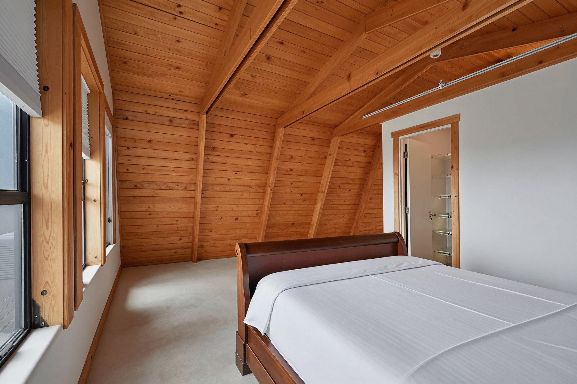 Vaulted wood-paneled ceiling with exposed beams, wood-frame windows, light-colored flooring, and a doorway revealing built-in shelving