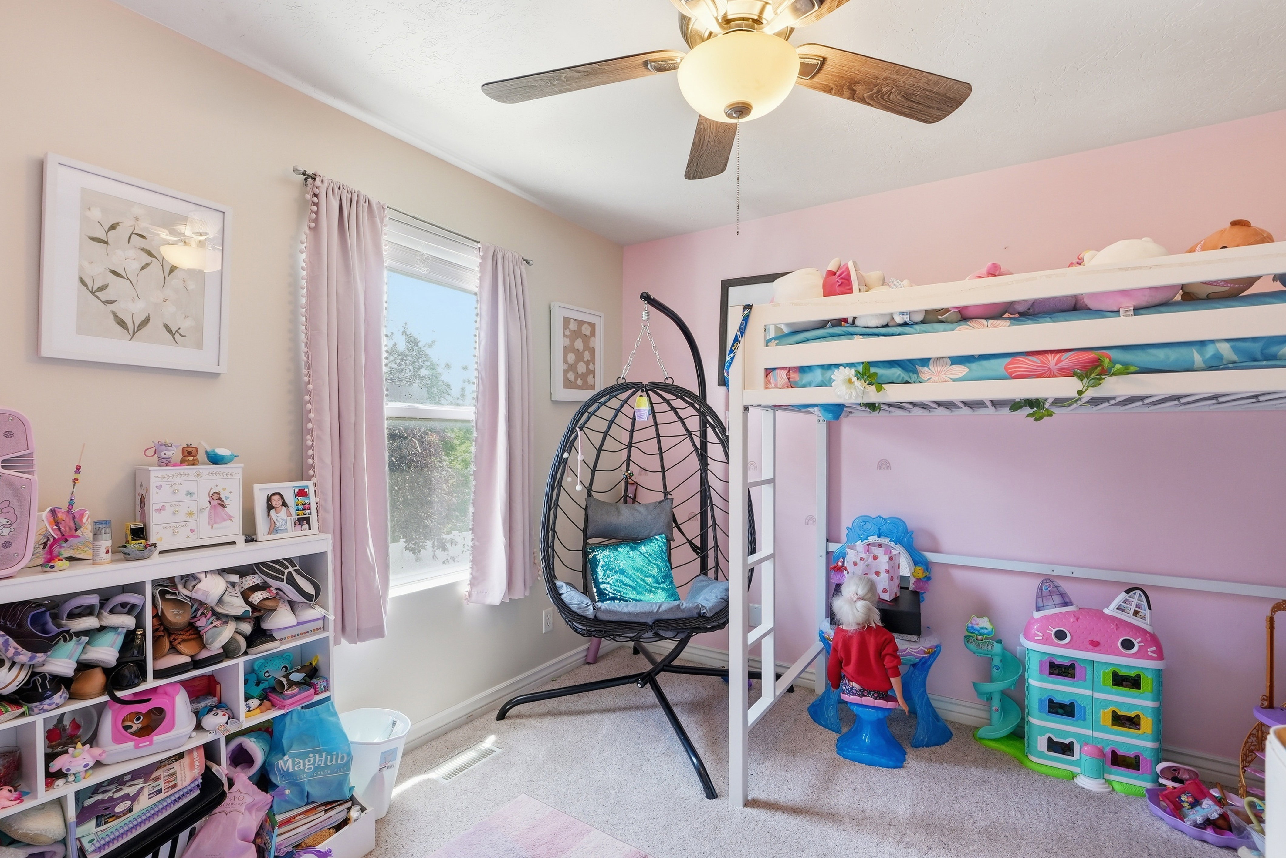 Carpeted room with a ceiling fan light fixture, a window with pink curtains, and light pink and beige wall finishes