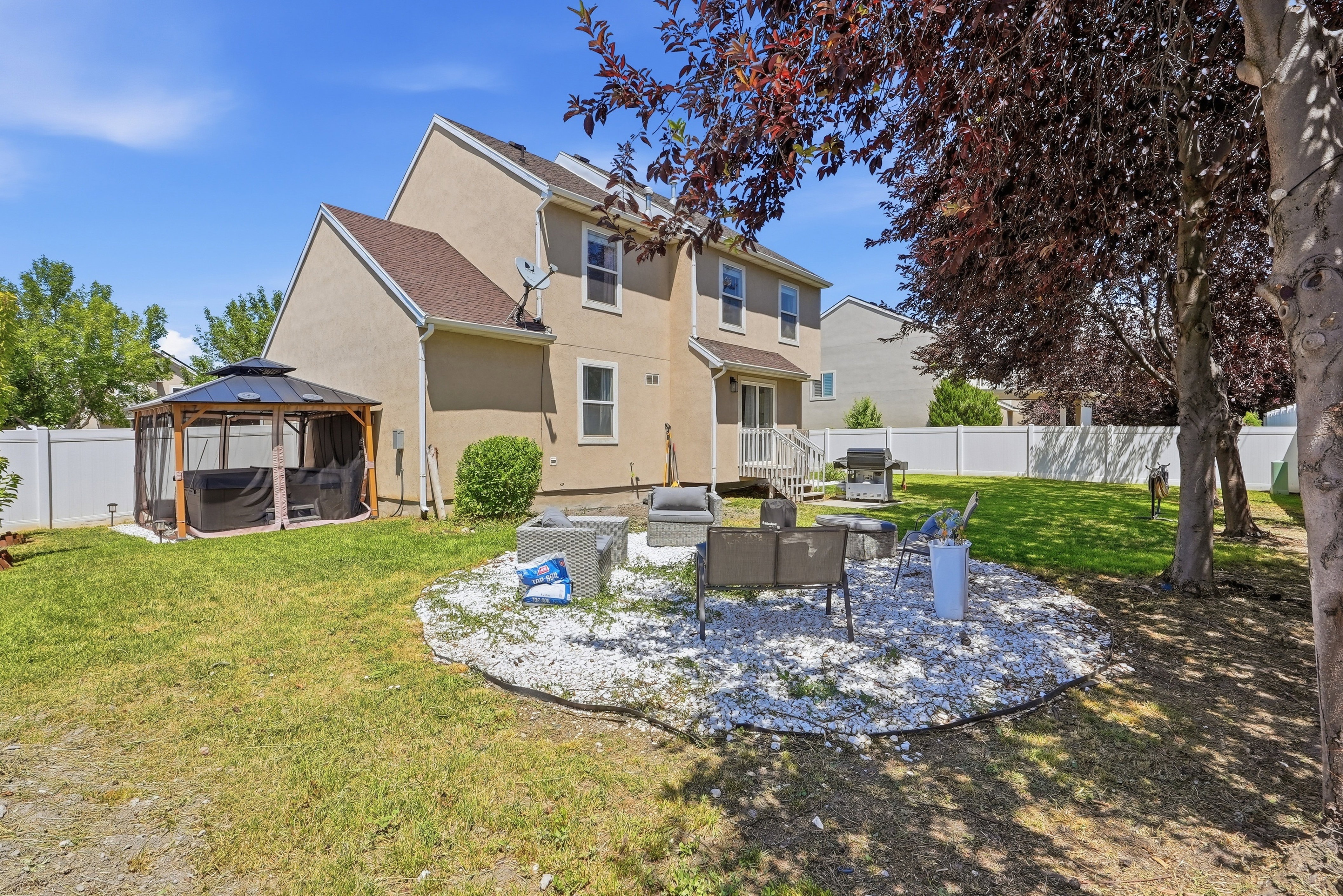Rear exterior featuring a spacious lawn, white perimeter fencing, and mature trees