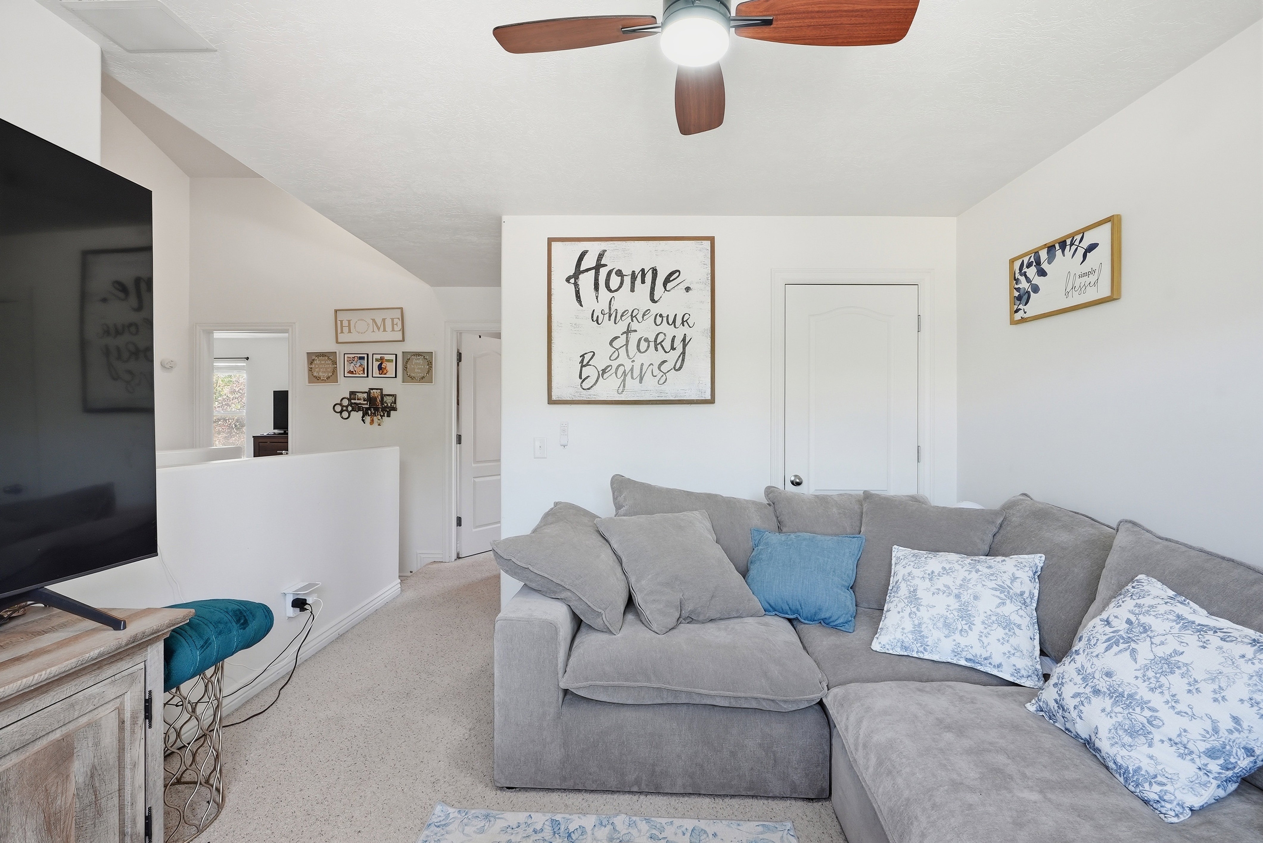 Carpeted living space featuring a ceiling fan with integrated lighting, white walls, and a partial wall separating areas