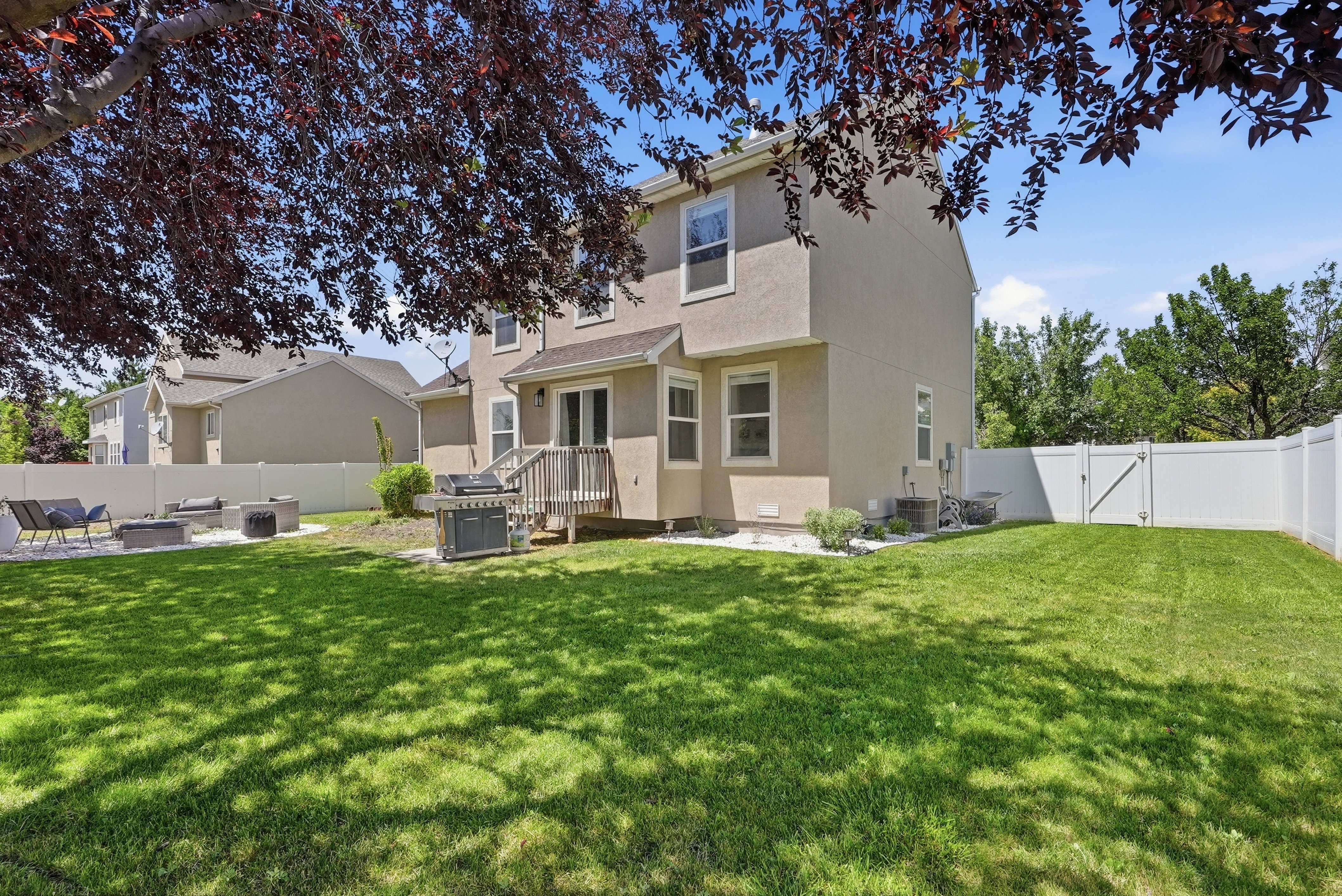 Expansive backyard featuring a manicured lawn, white privacy fencing, a multi-level deck, and a concrete patio with built-in features