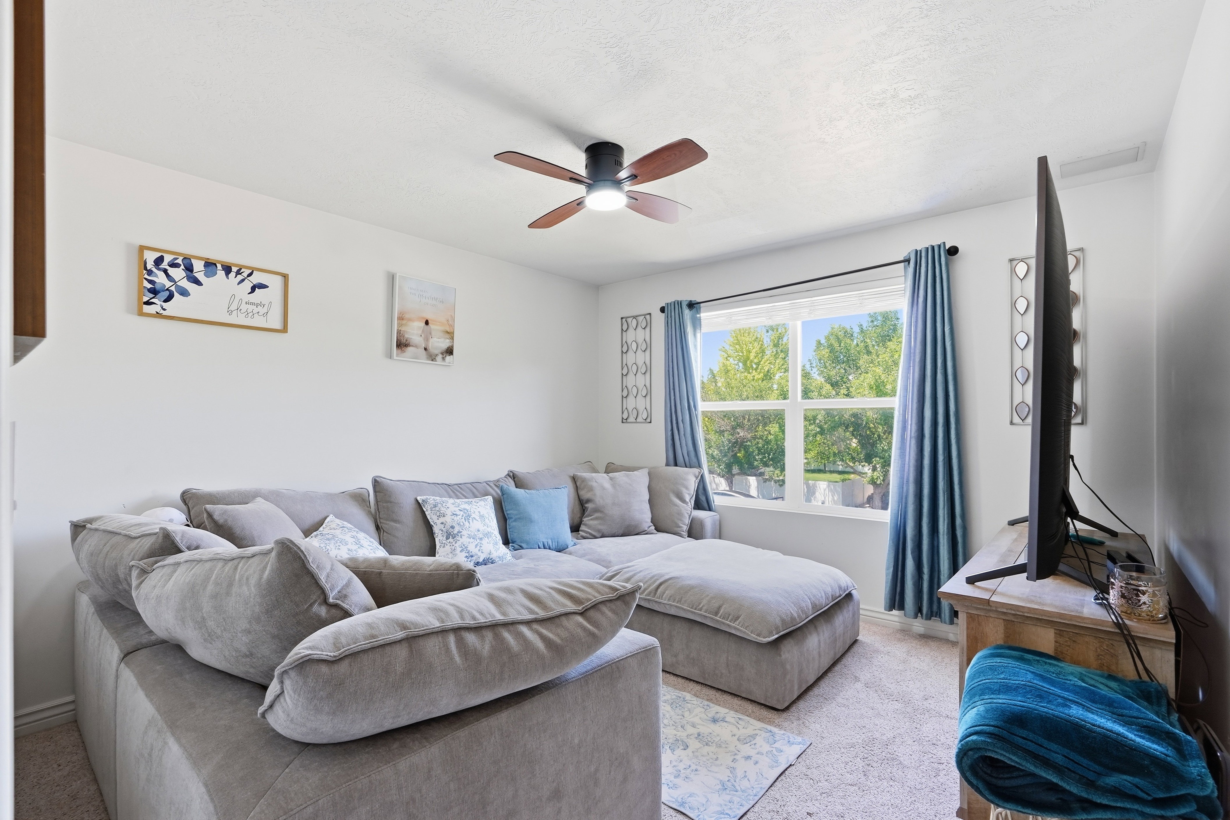 Bright living area featuring a large window, carpet flooring, a ceiling fan with integrated lighting, and white walls